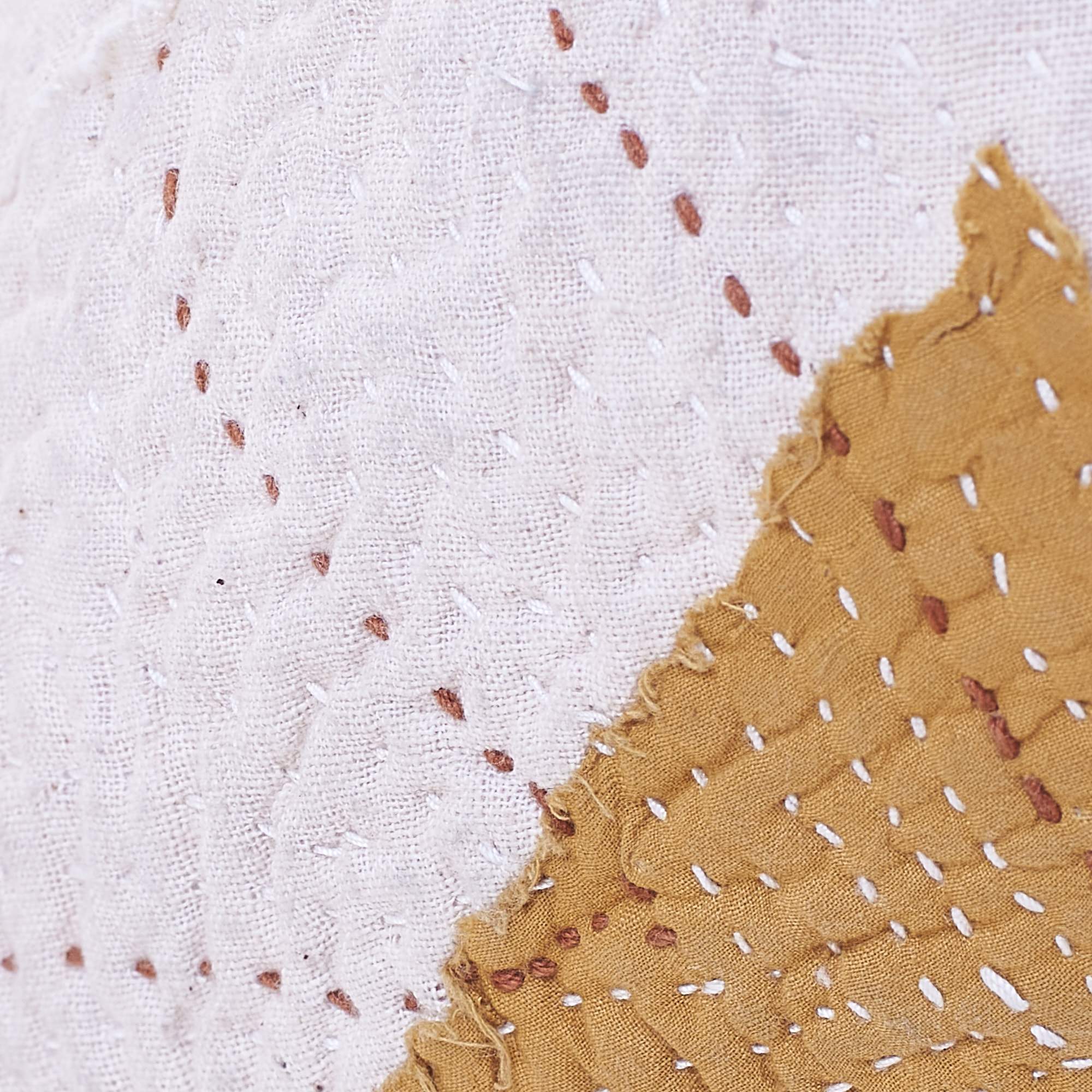 Close-up of white fabric with brown thread stitches on a white background
