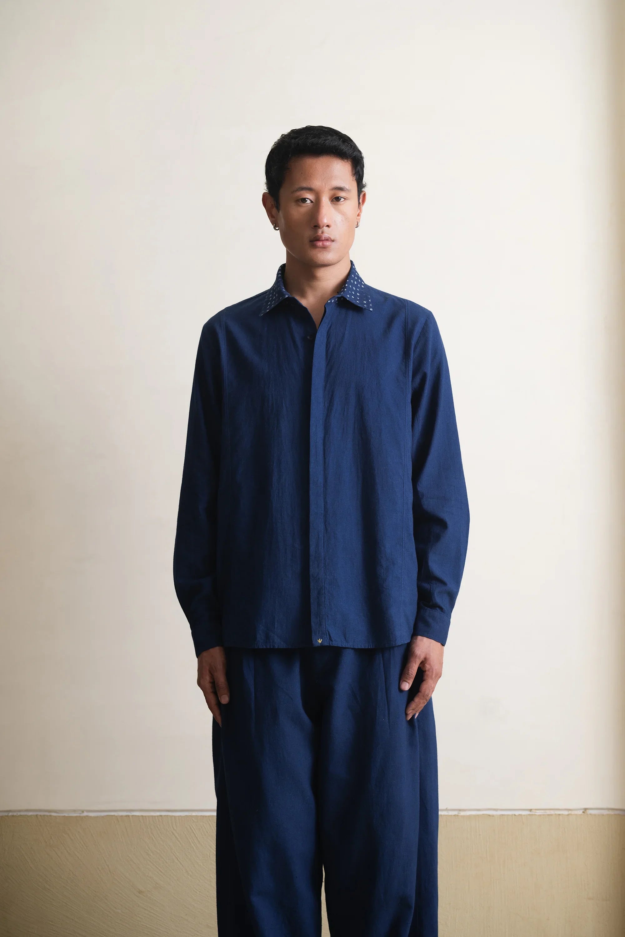 Man wearing a blue shirt and pants against a plain background