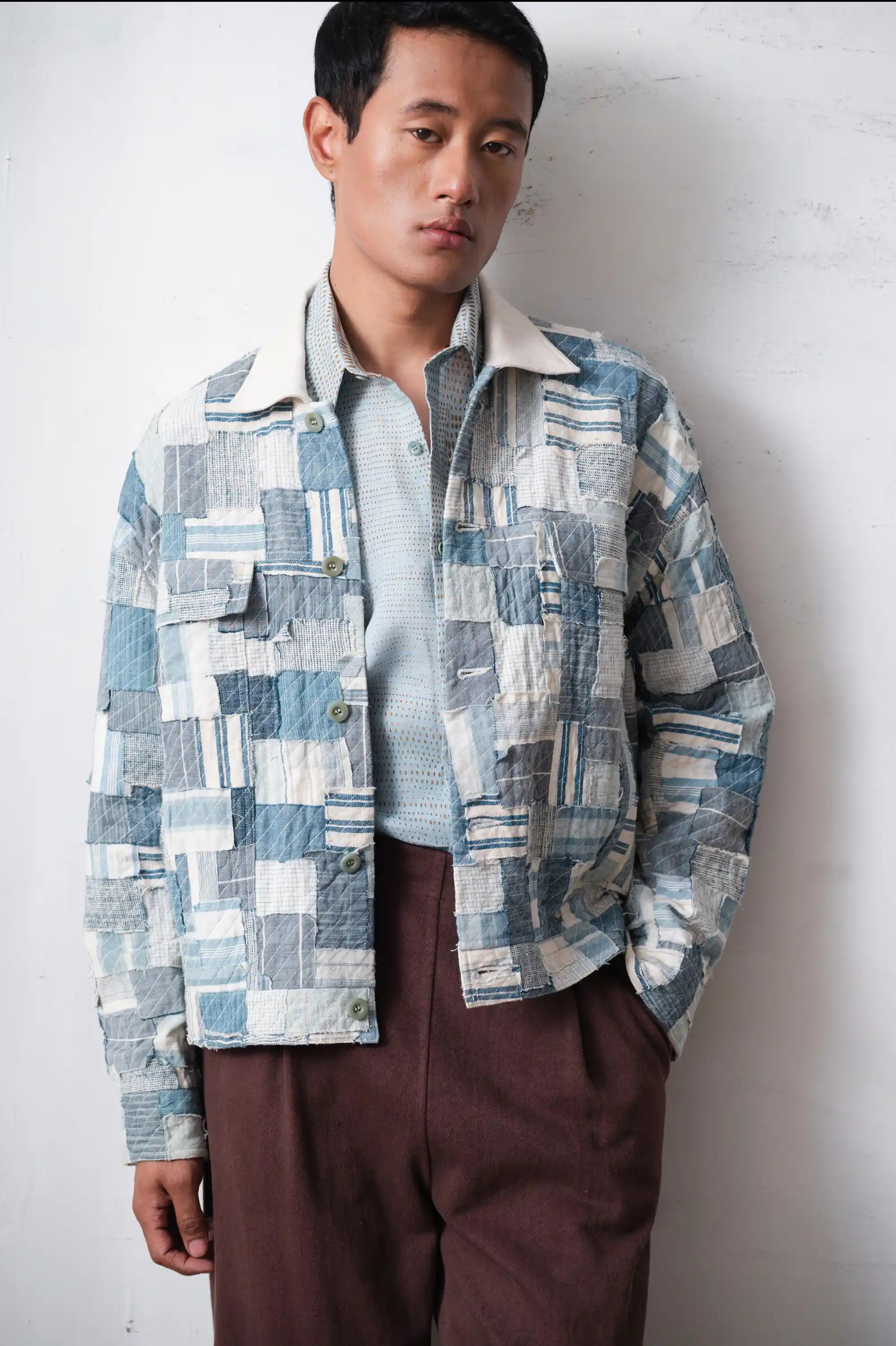 Man wearing a patchwork jacket against a light grey background