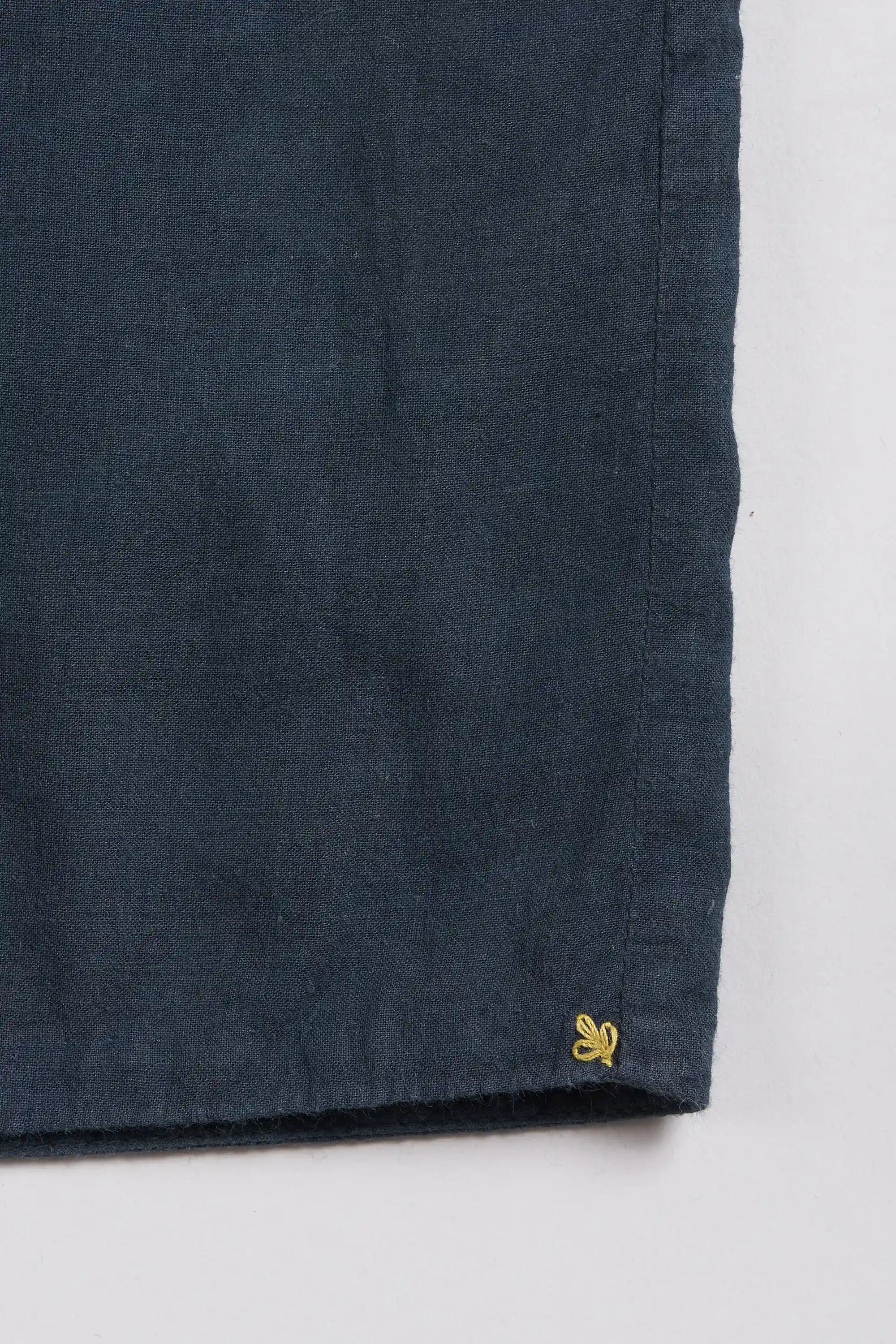 Close-up of a dark midnight indigo fabric product corner with a small yellow embroidered logo.