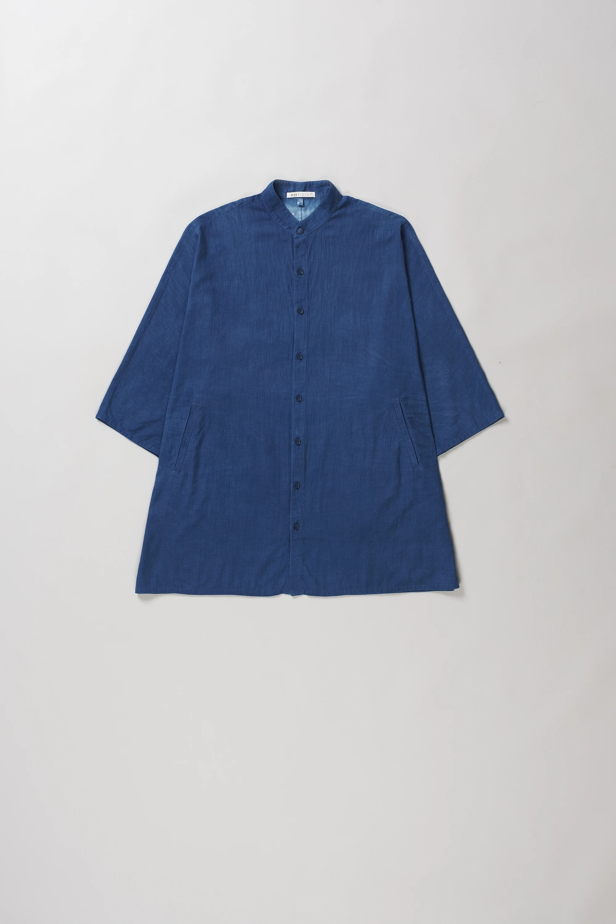 A medium indigo half-sleeve button-up shirt with a mandarin collar, laid flat against a light grey background.