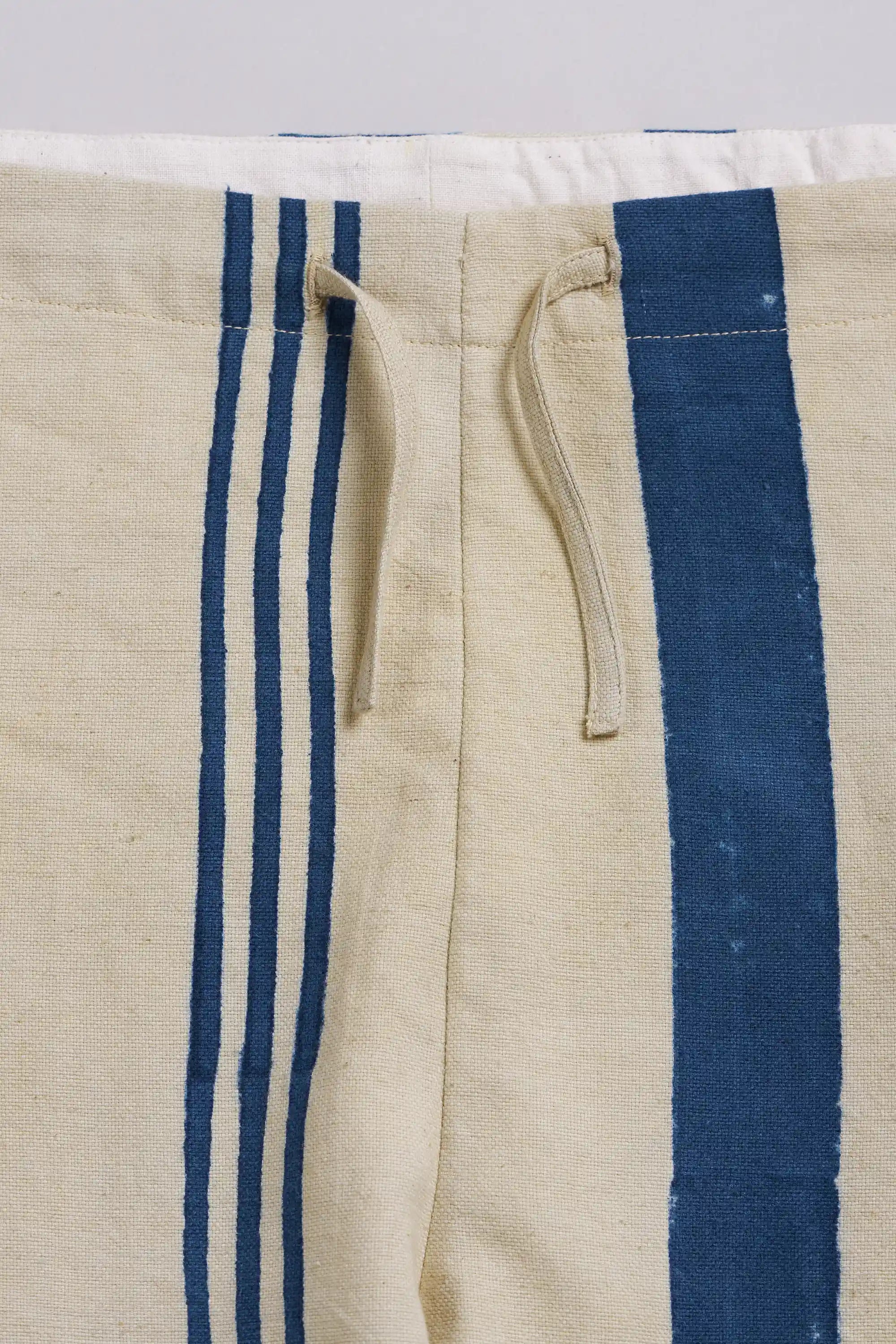 Close-up of a pant featuring bold vertical blue stripes and a matching beige drawstring.