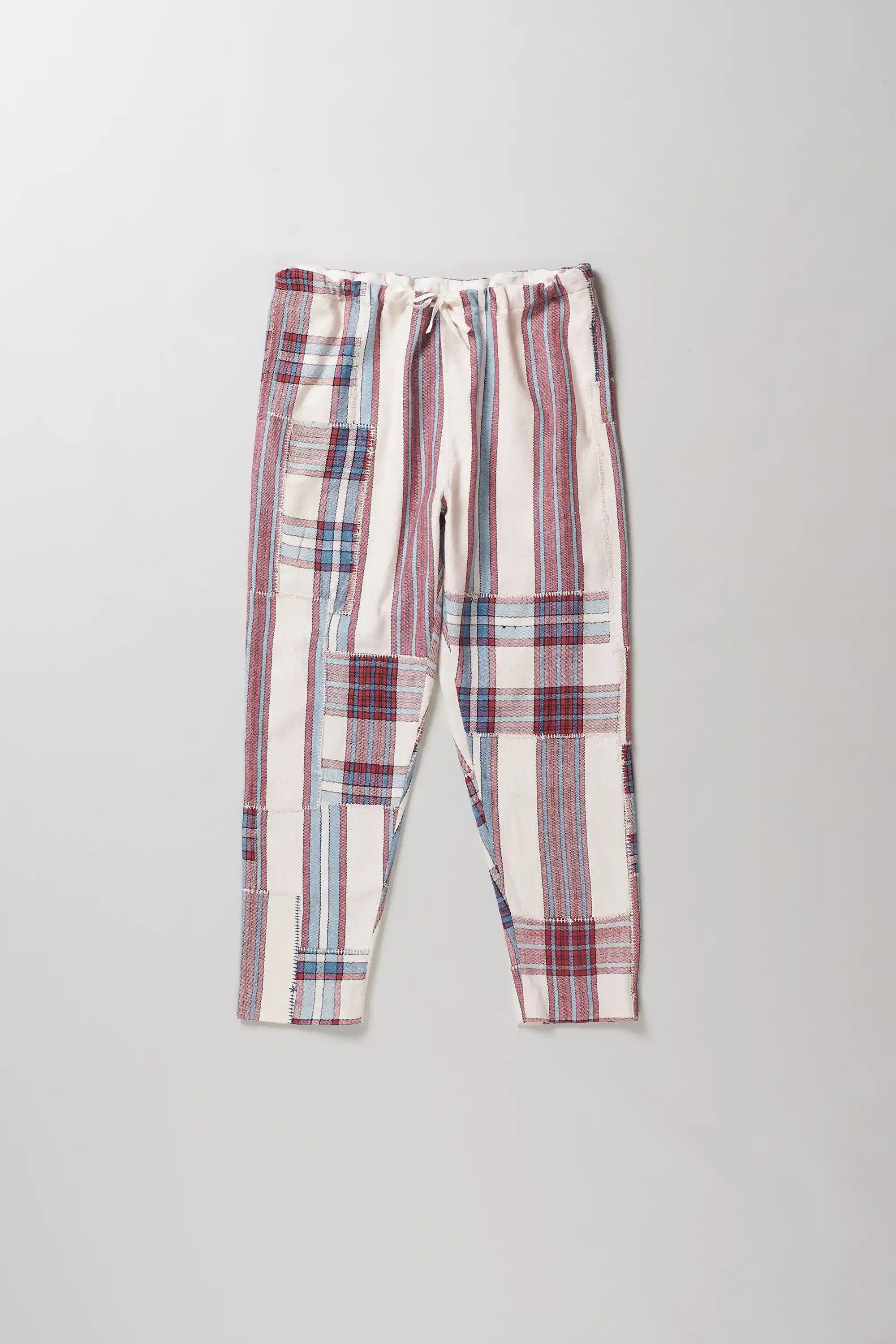 A pair of patchwork pants in pink, red, blue, and white, featuring a drawstring waistband, laid flat against a light grey background.