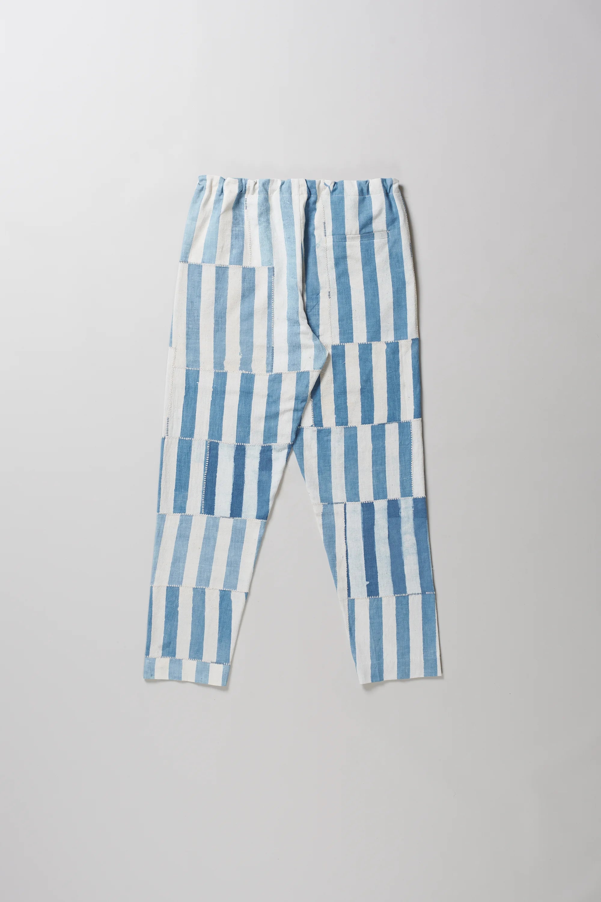 Back light indigo and white vertically striped cropped pants with a drawstring waist, laid flat on a light grey background.