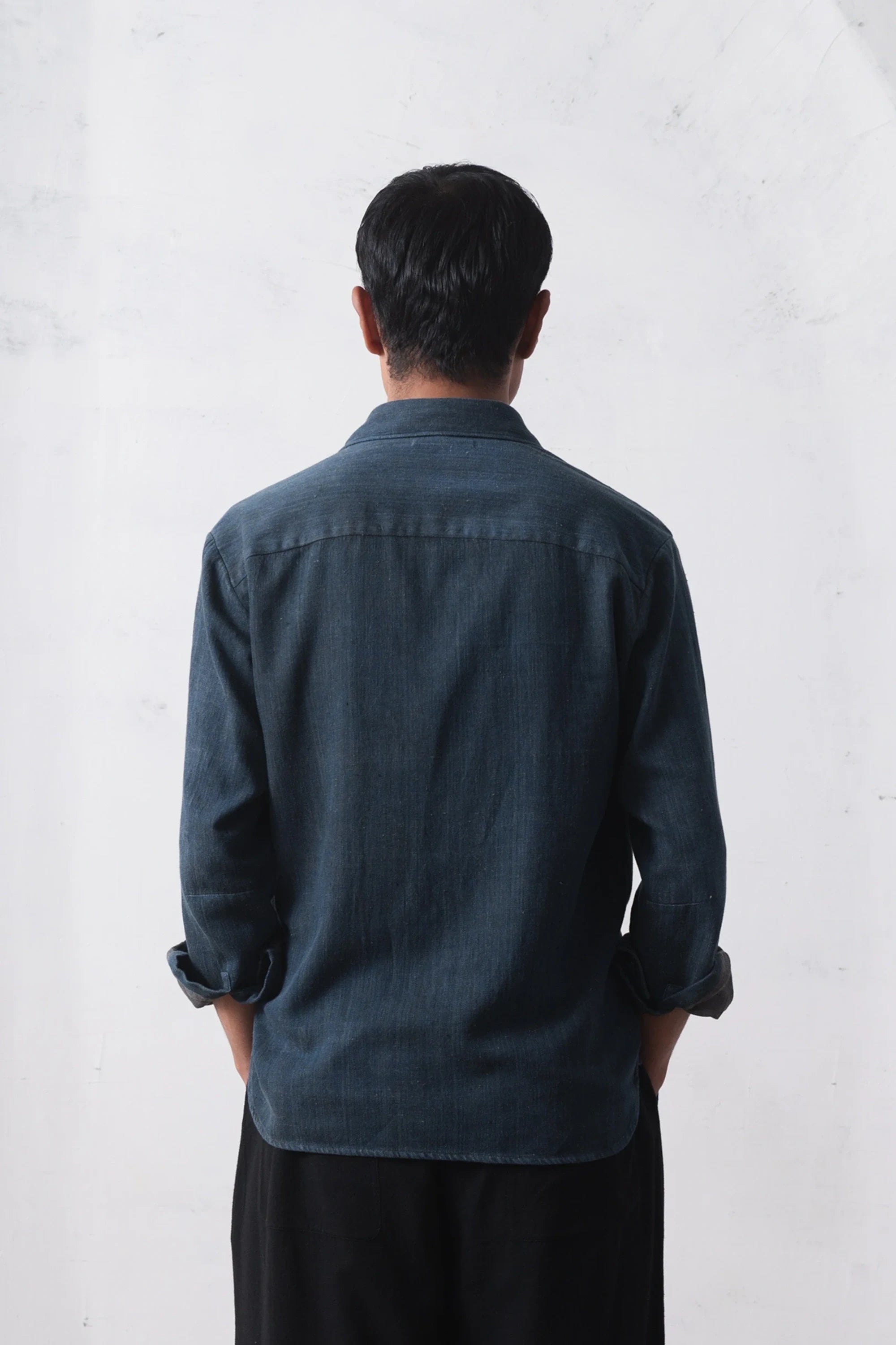 Back shot of a person wearing a indigo denim shirt on a white background