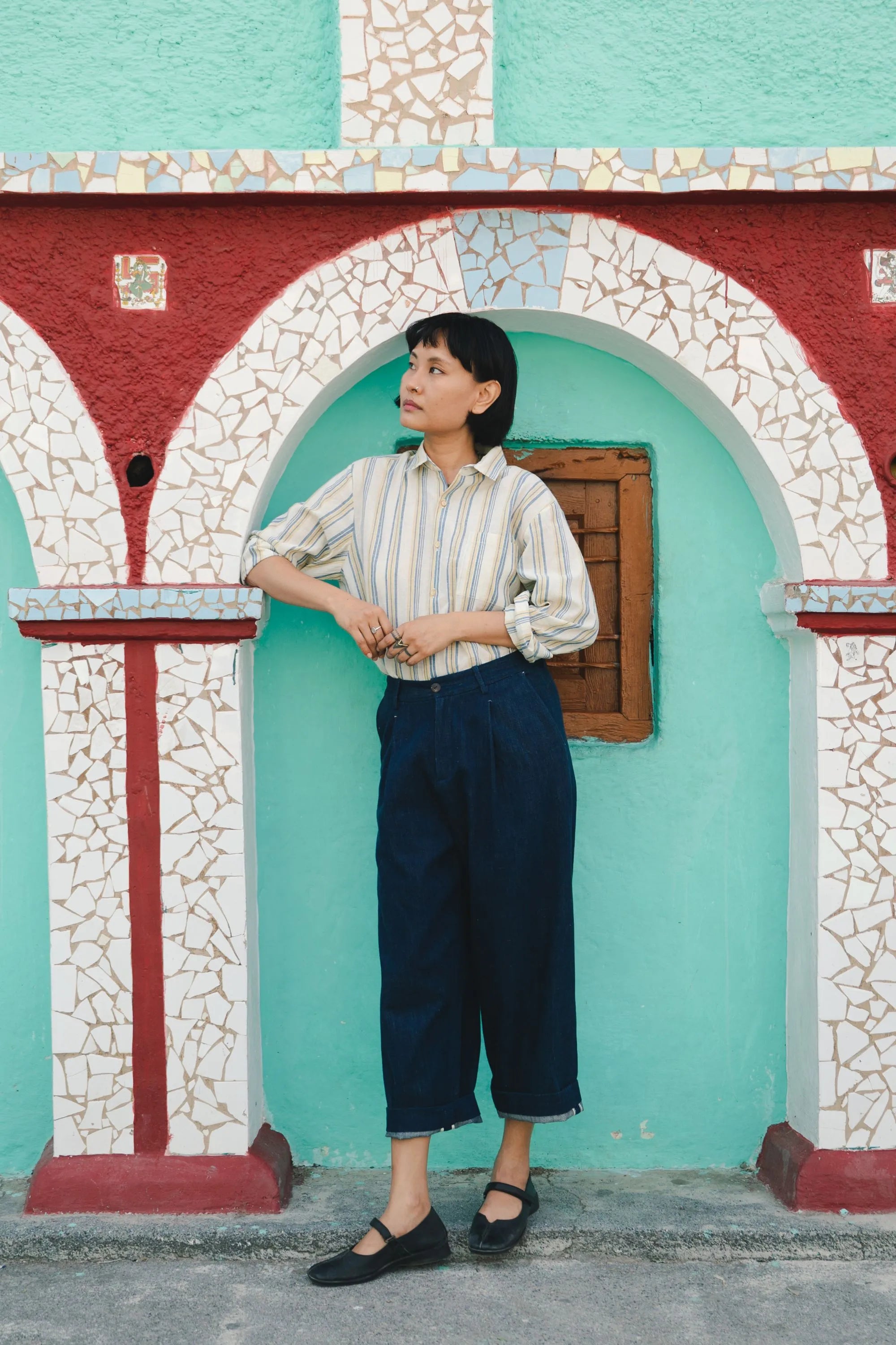 A woman wearing indigo pant and cotton shirt standing in front of a colorful archway with mosaic patterns