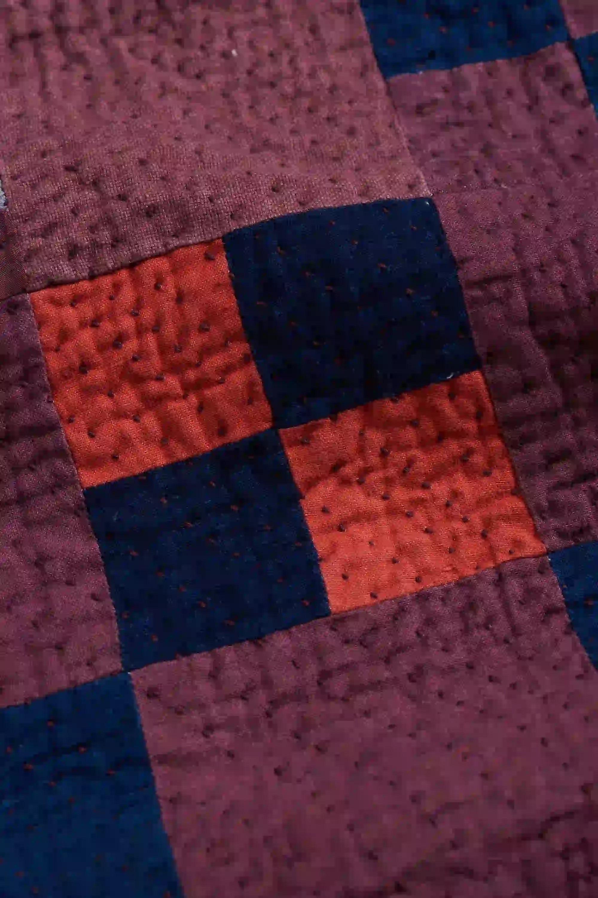 Close-up of a quilt with a checkered pattern in red, blue, and brown.