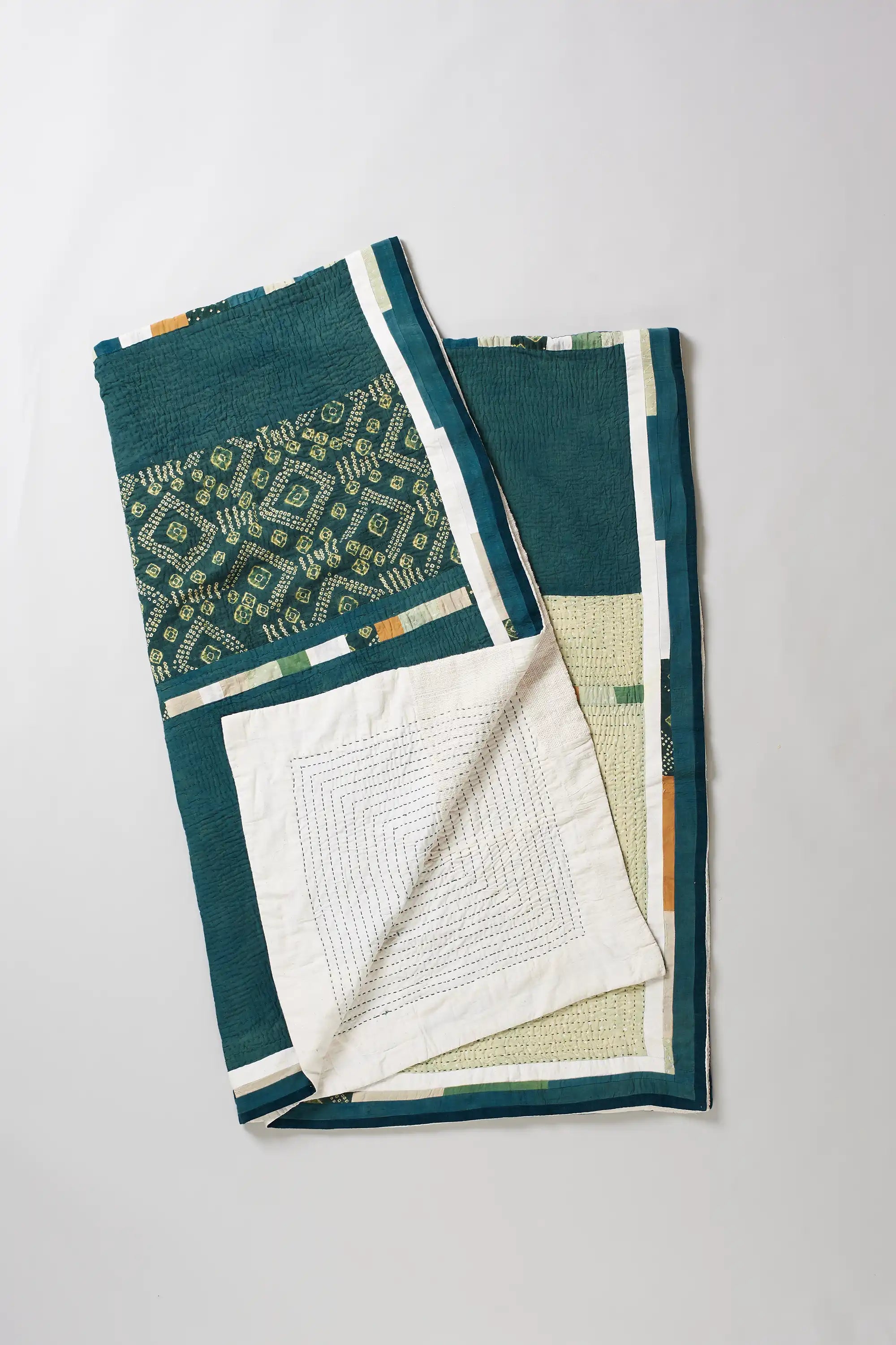 Folded turf green quilt with kantha and bandhani work on light grey background