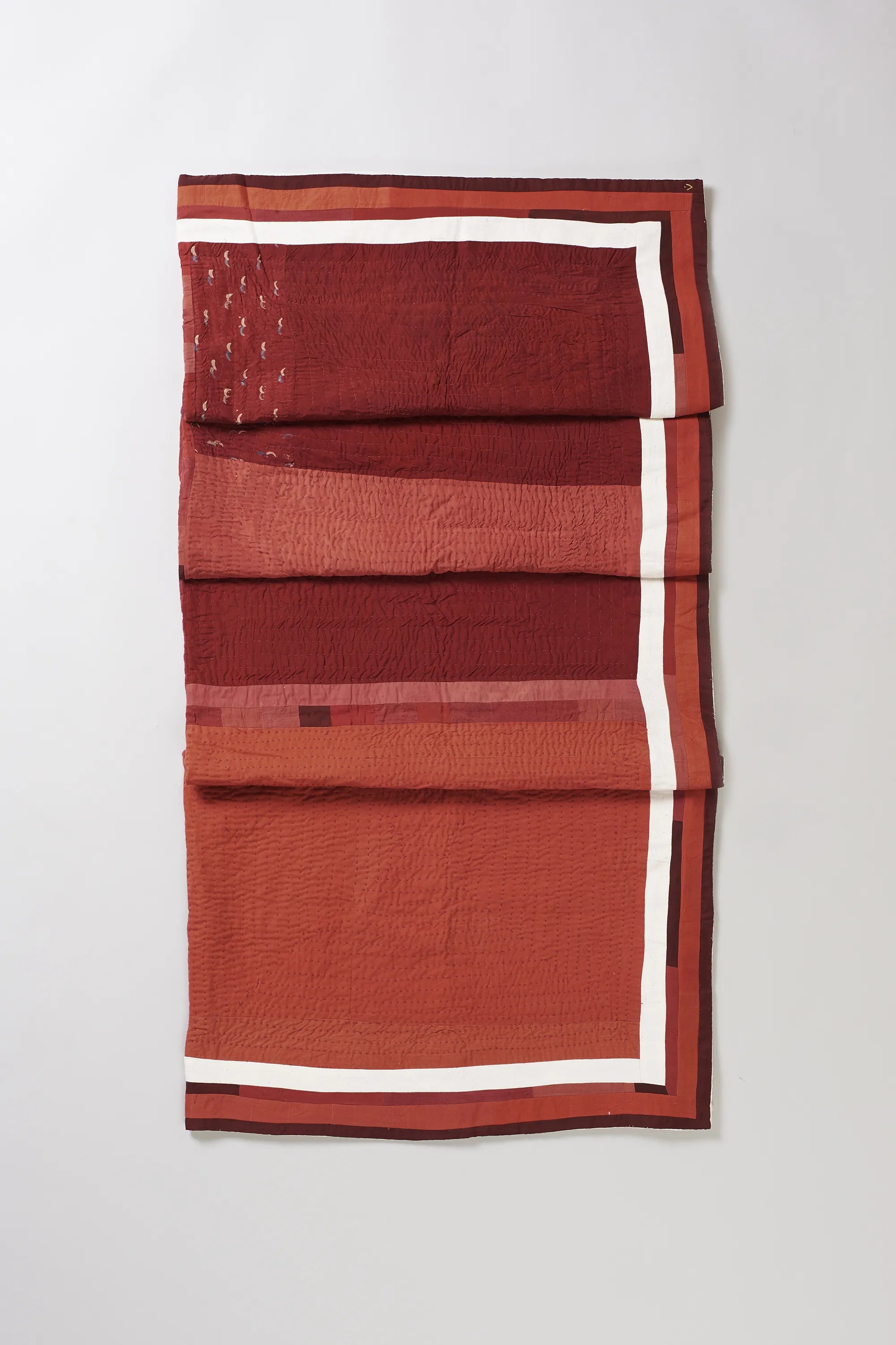 Folded red quilt with white border on a light grey background