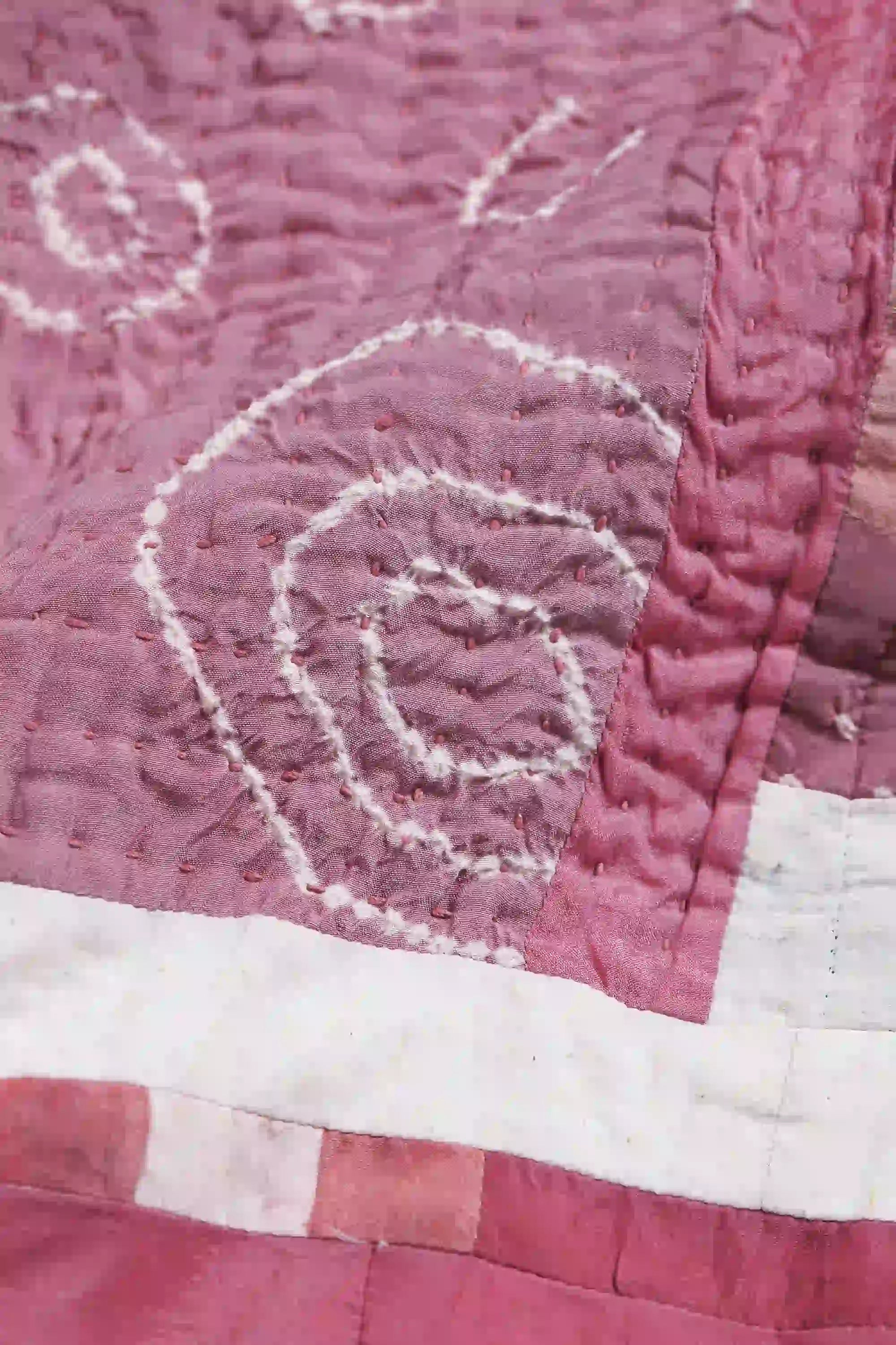 Close-up of a quilt with intricate white embroidery on a pink background