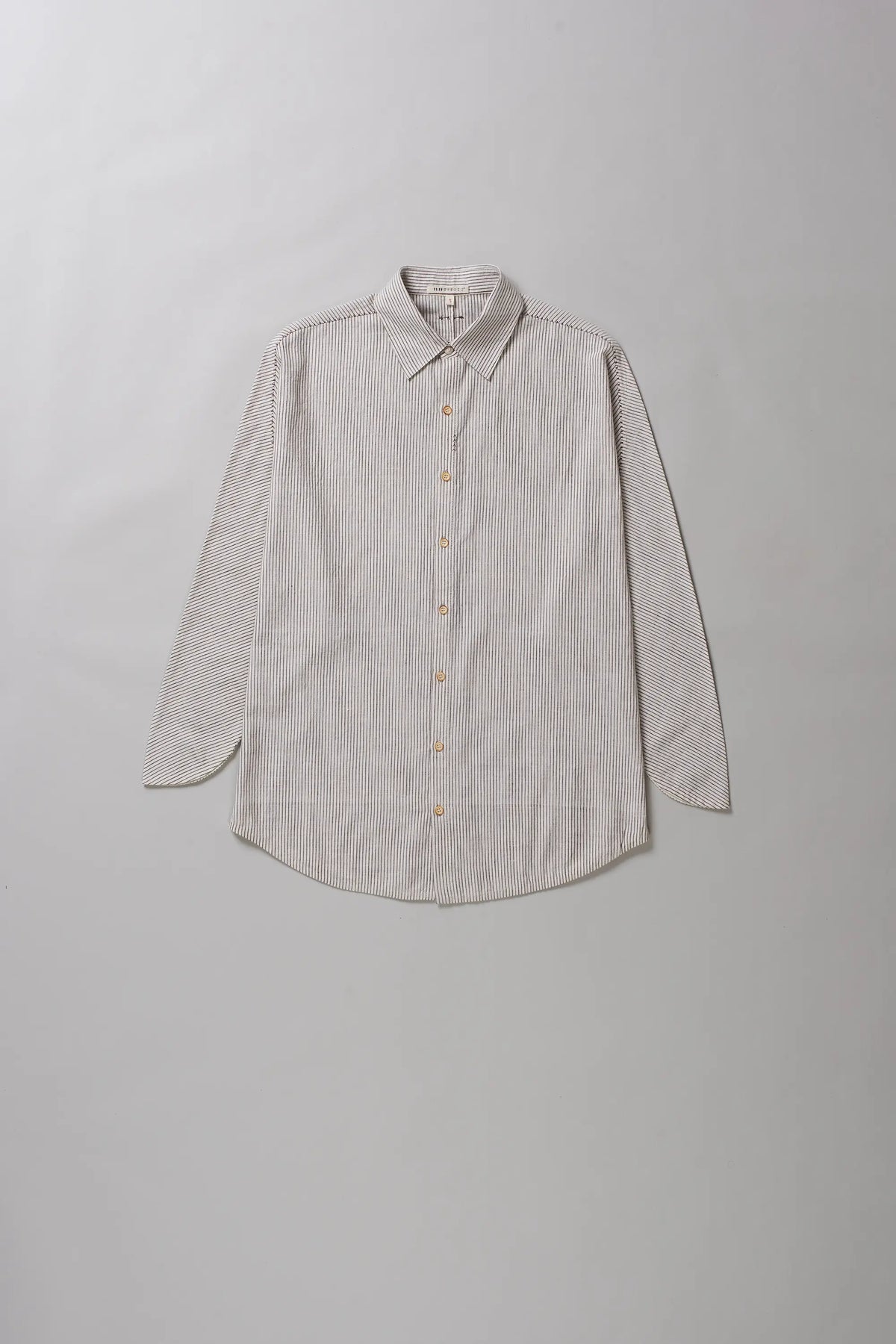 A light beige long-sleeve button-up shirt with a subtle textured weave, laid flat against a neutral grey background.