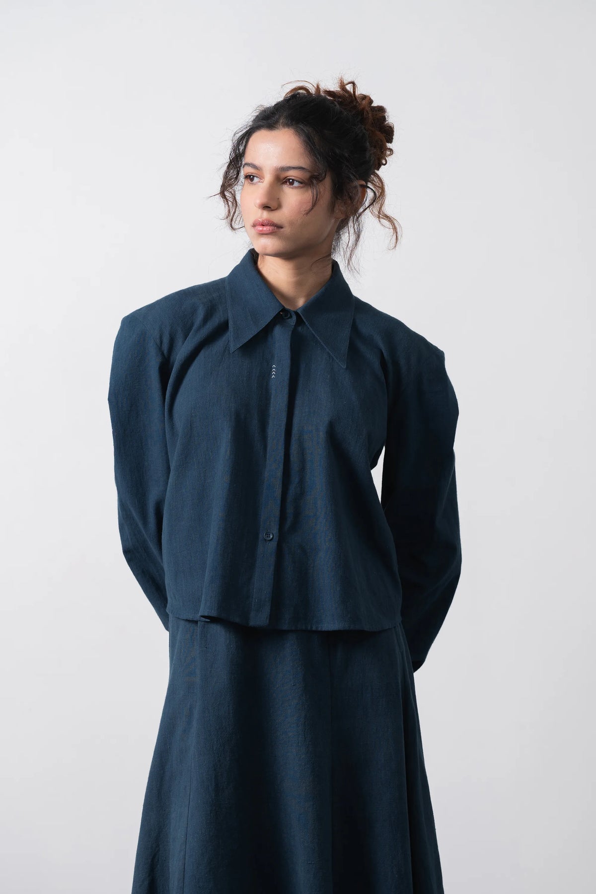 A model wearing a space blue long-sleeve collared shirt and matching skirt, standing against a plain grey background.