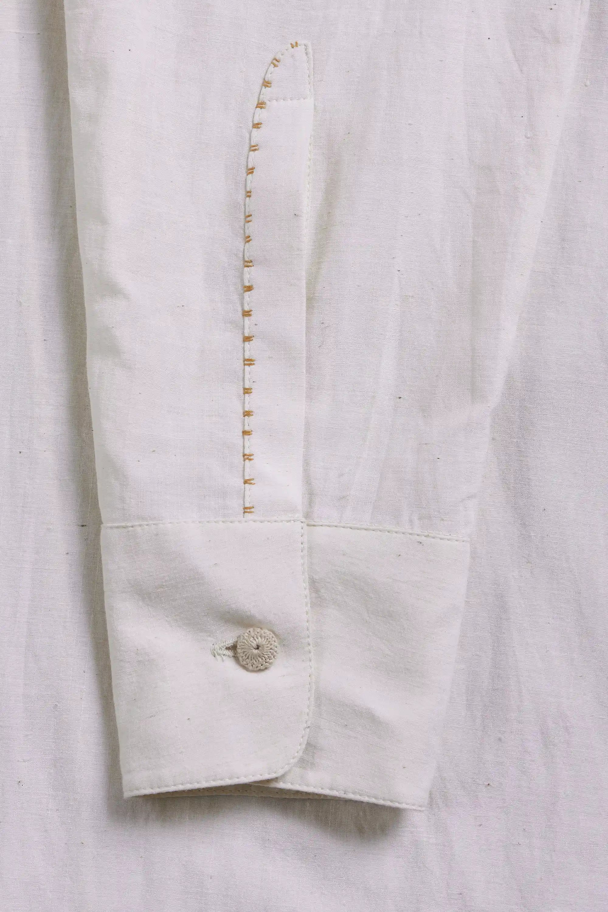 Close-up of cuff of a sleeve with a single button and a vertical decorative stitched seam.
