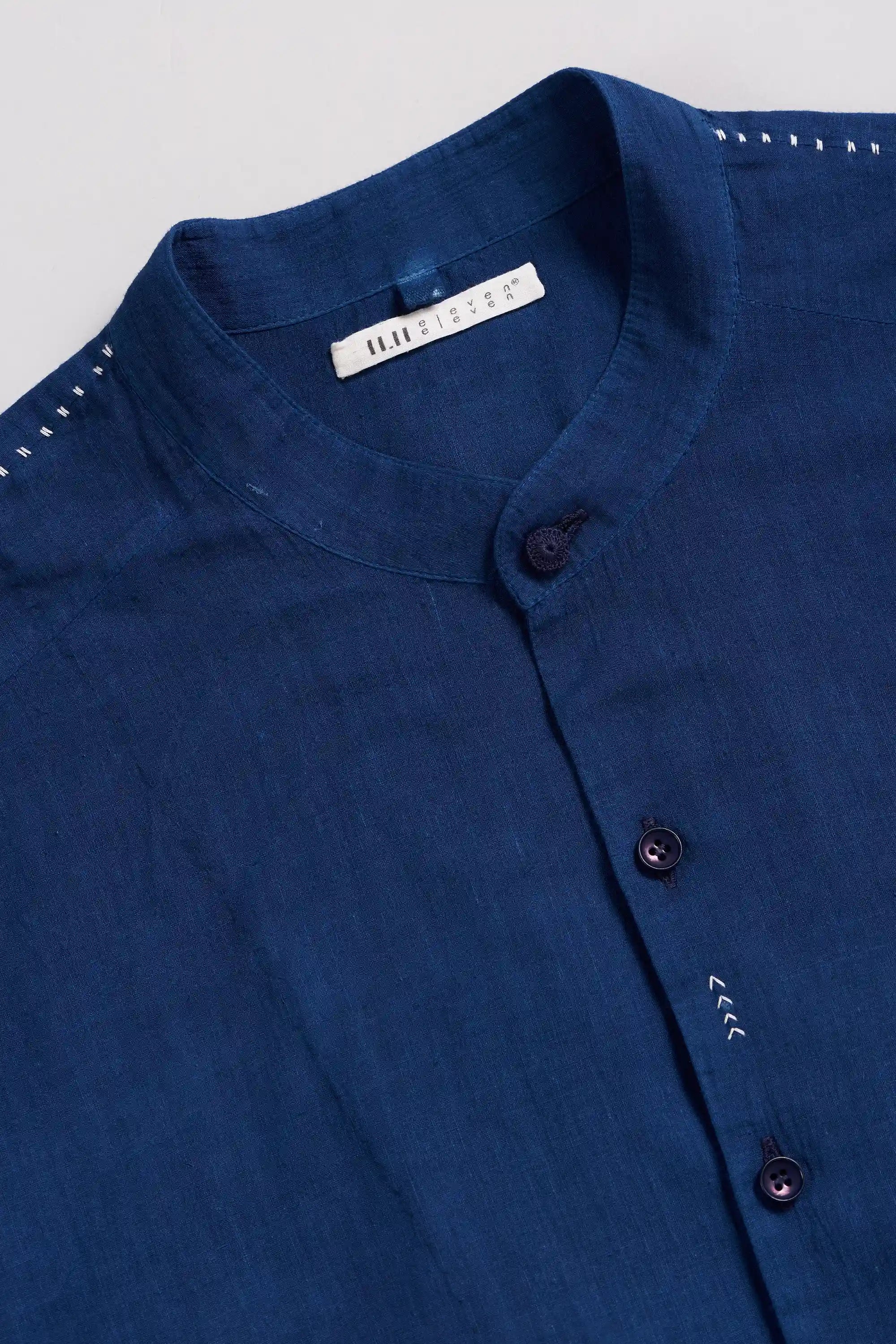 Close-up of a blue shirt with band collar and buttons with a brand label on a light grey background