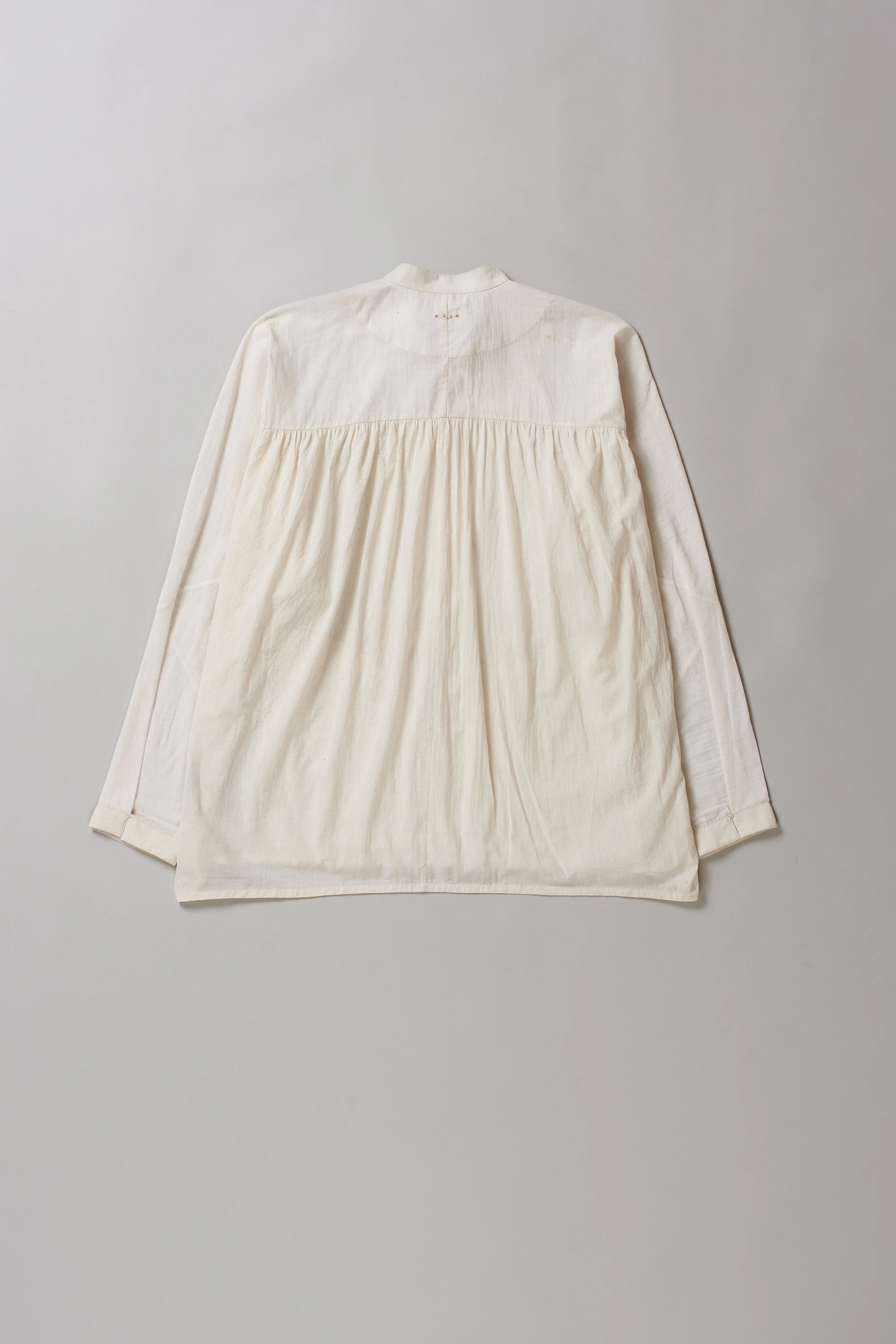 Back image of ecru cotton shirt with hand detailing on a grey background