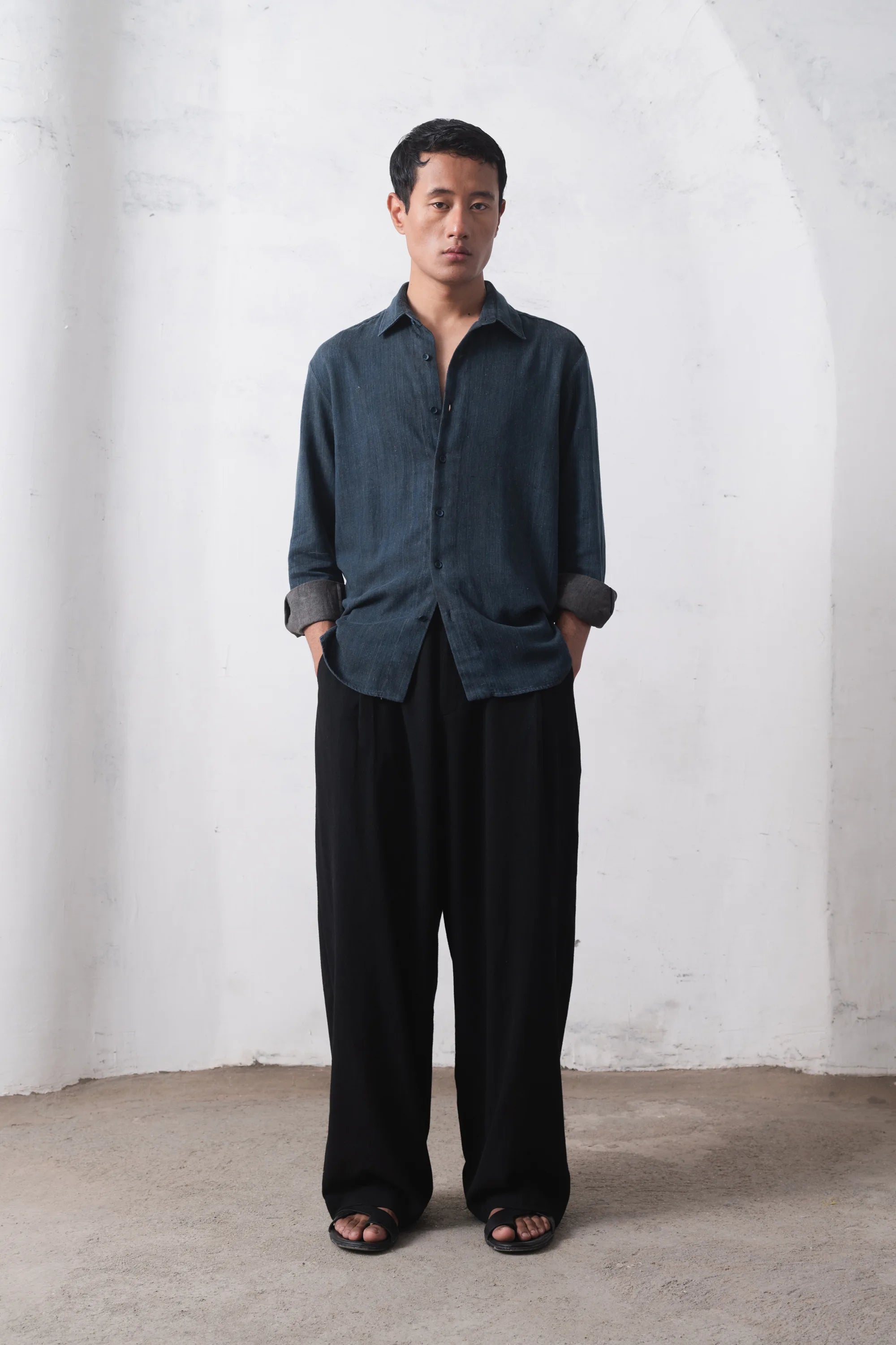 Man wearing a indigo shirt and black pants on a white wall