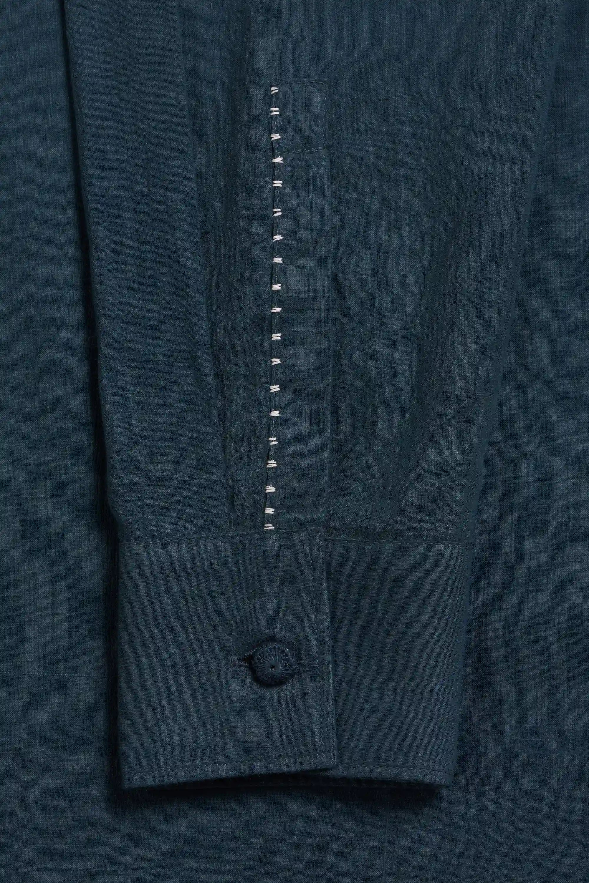 Close-up of cuff of a sleeve with a single button and a vertical decorative stitched seam.