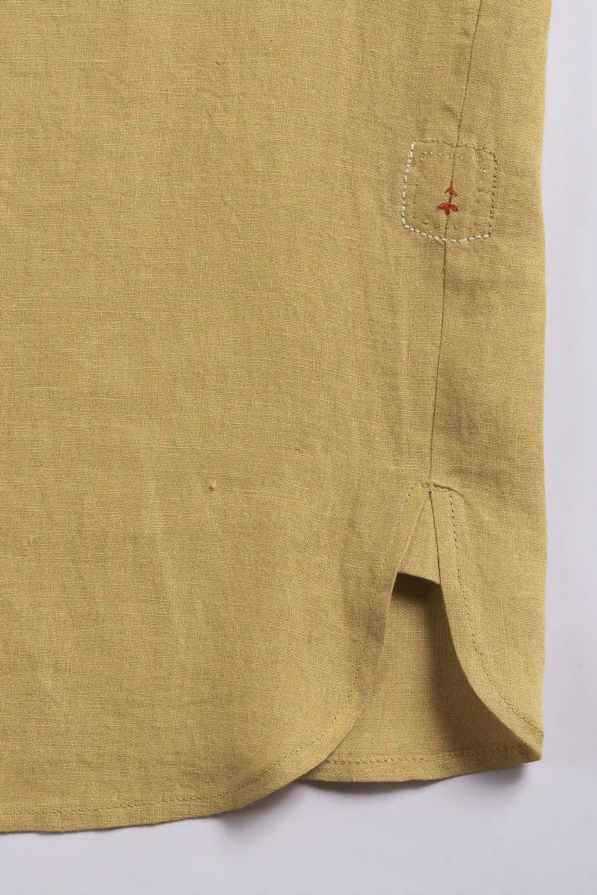 Close-up of a ochre yellow shirt with red small pehchanbox on a light grey background