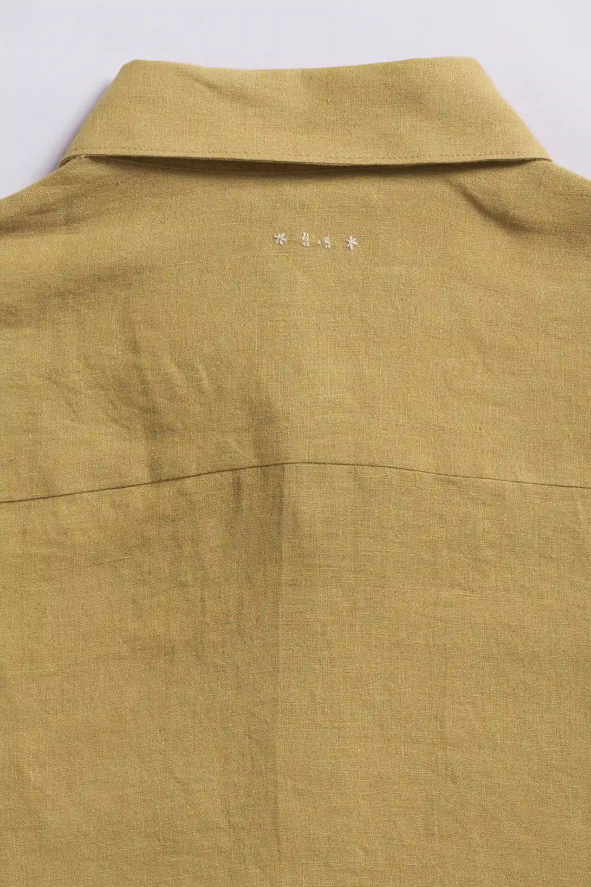 Close-up of a ochre yellow shirt with a collar and hand detailing on a light grey background