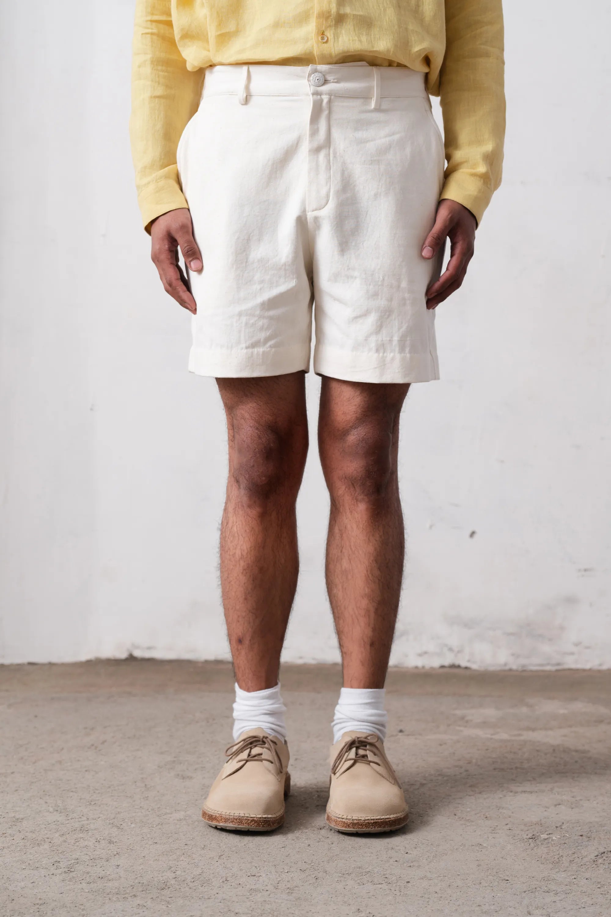 Person wearing white shorts, a yellow shirt, and beige shoes against a plain background