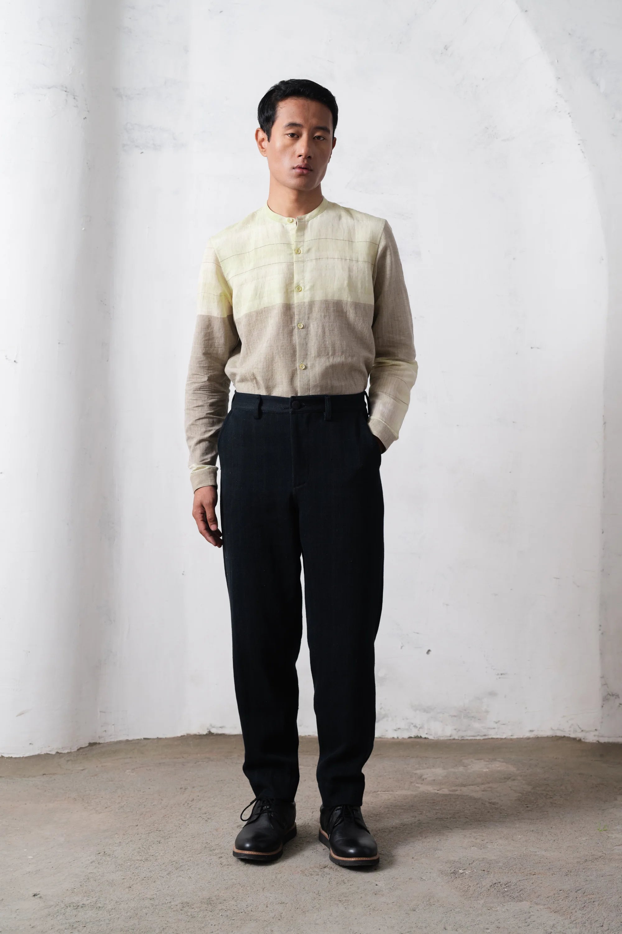 Man wearing a light-colored shirt and midnight indigo pants against a light grey wall