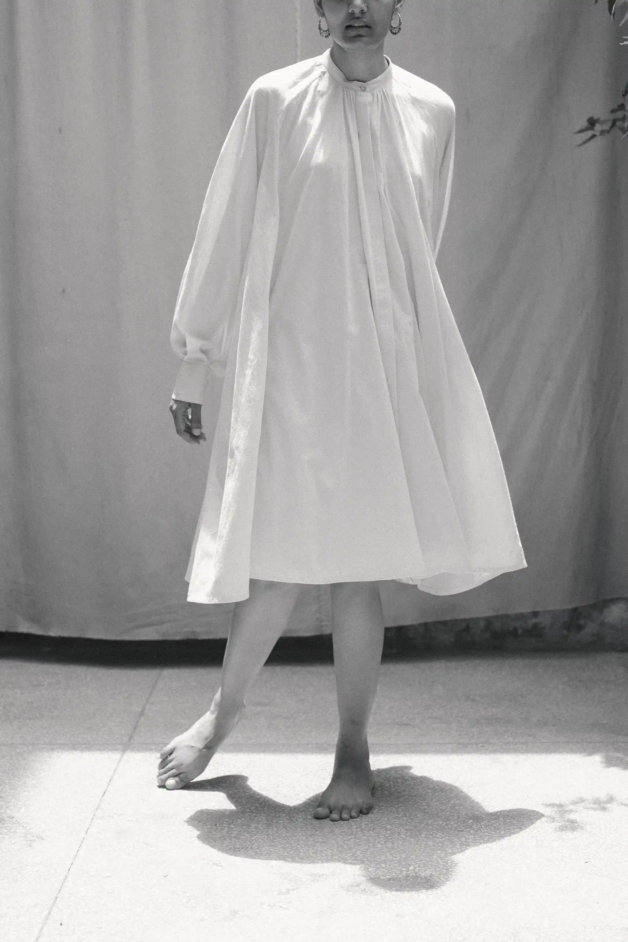 Person wearing a ecru cotton dress standing against a plain background