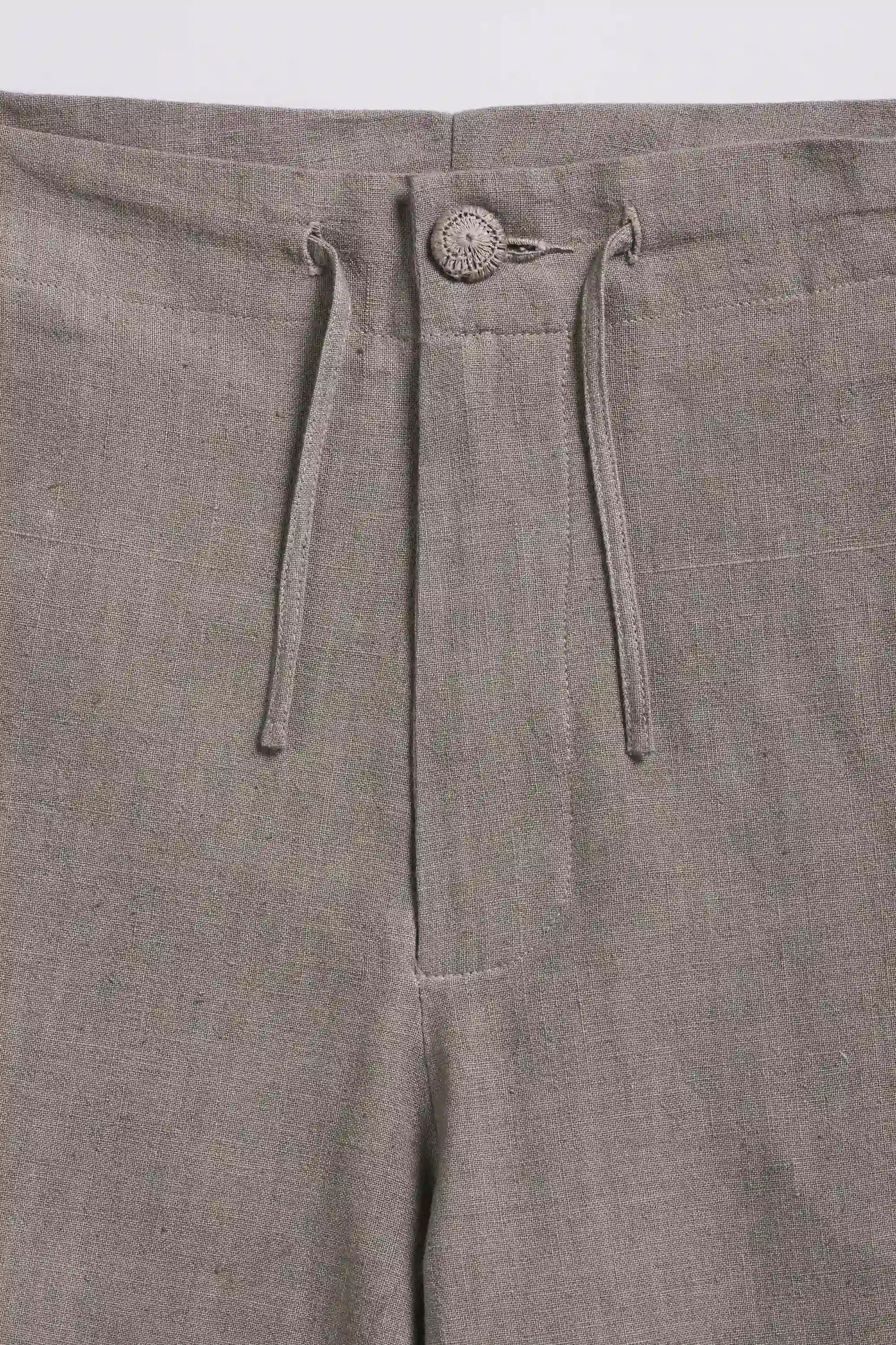 Close-up of ash grey pants with drawstring and button detail on a light grey background
