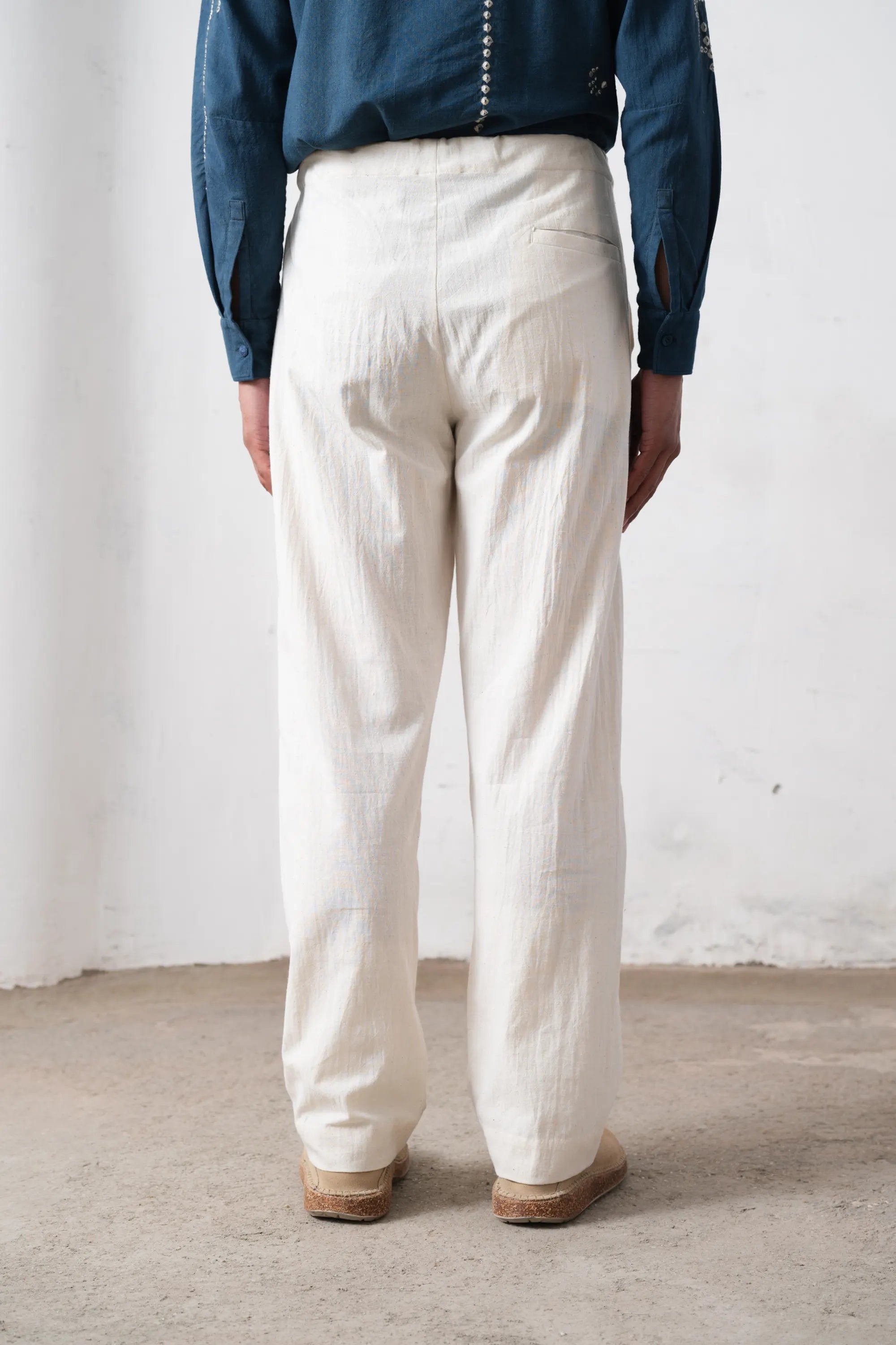 Back shot of a person wearing white pants and a blue shirt against a plain background