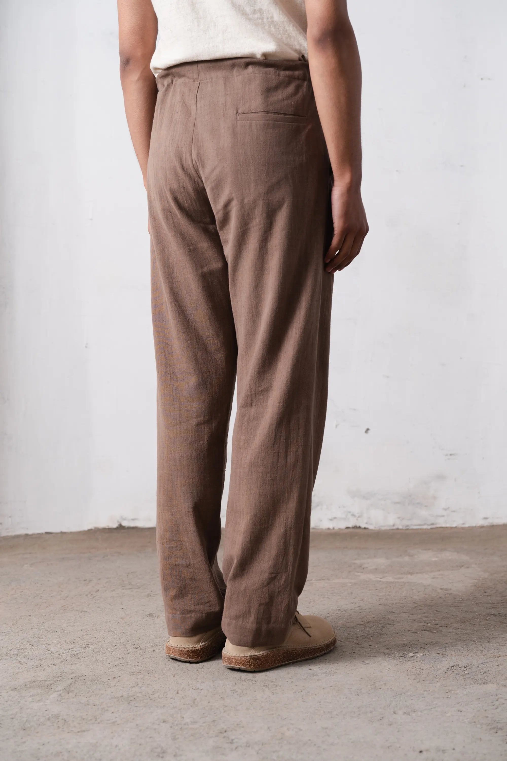 Back shot of a person wearing brown pants against a light grey wall