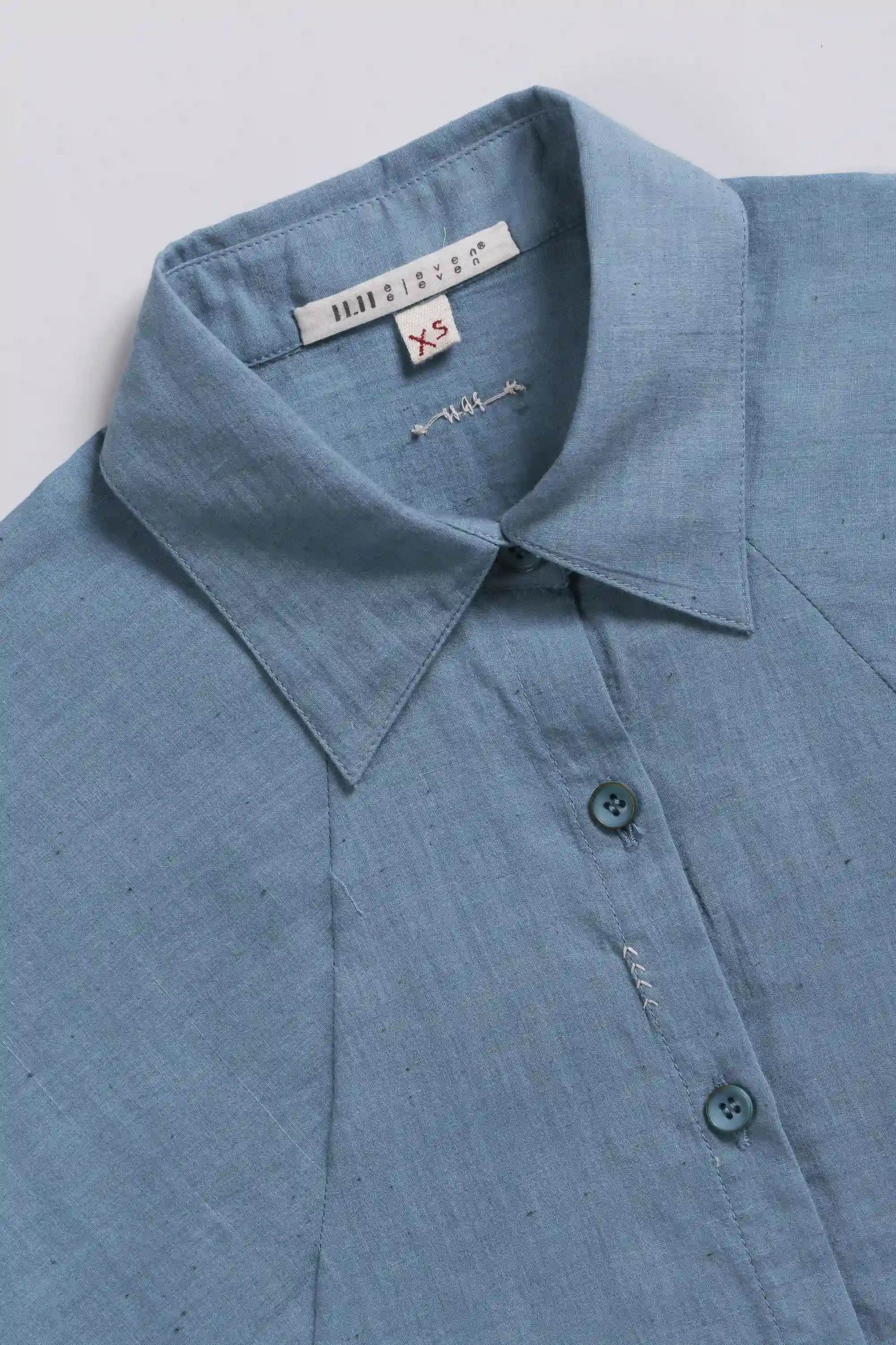 Close-up of a blue shirt collar with buttons brand label on a light grey background