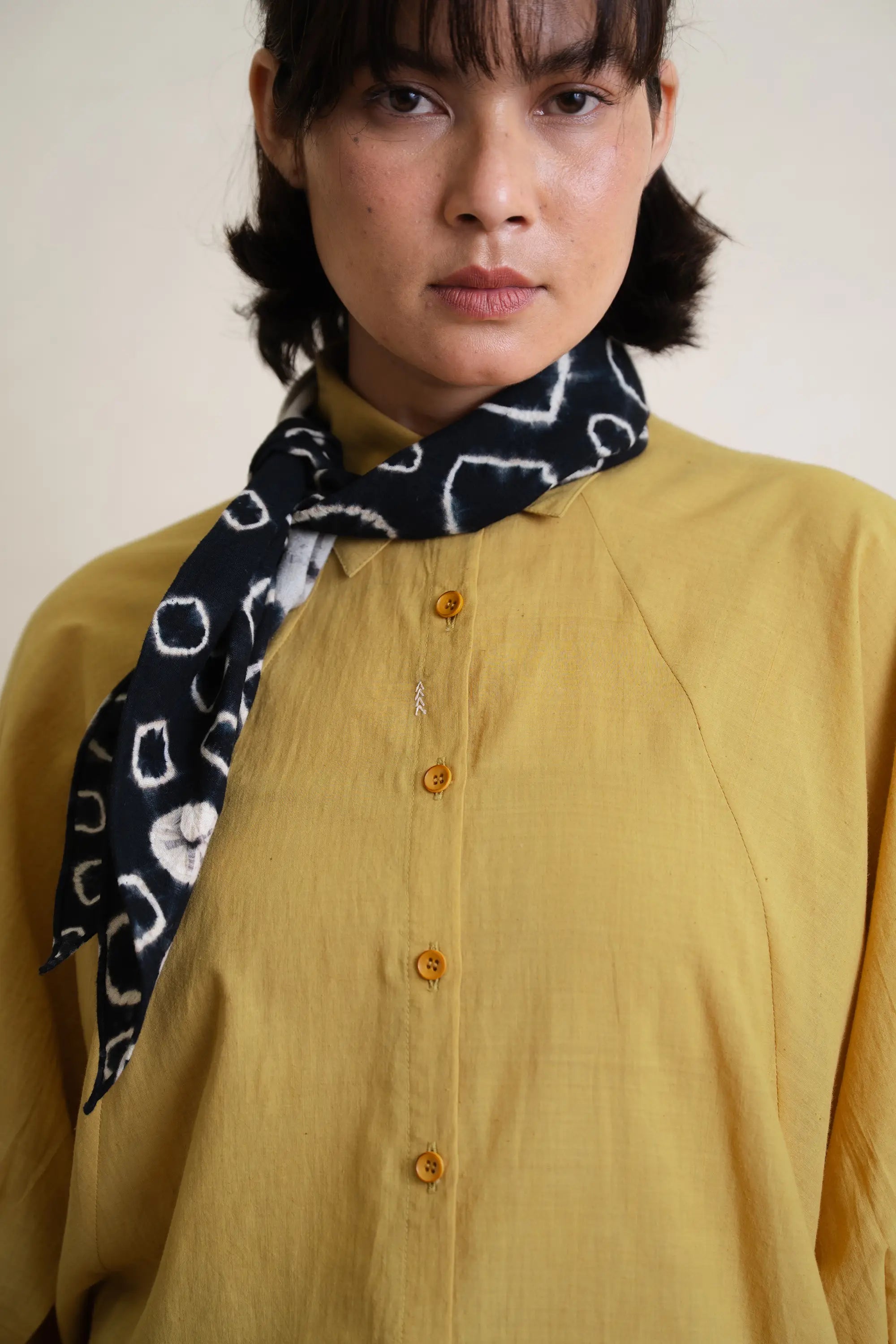 Person wearing a yellow shirt and a black and white patterned scarf against a plain background