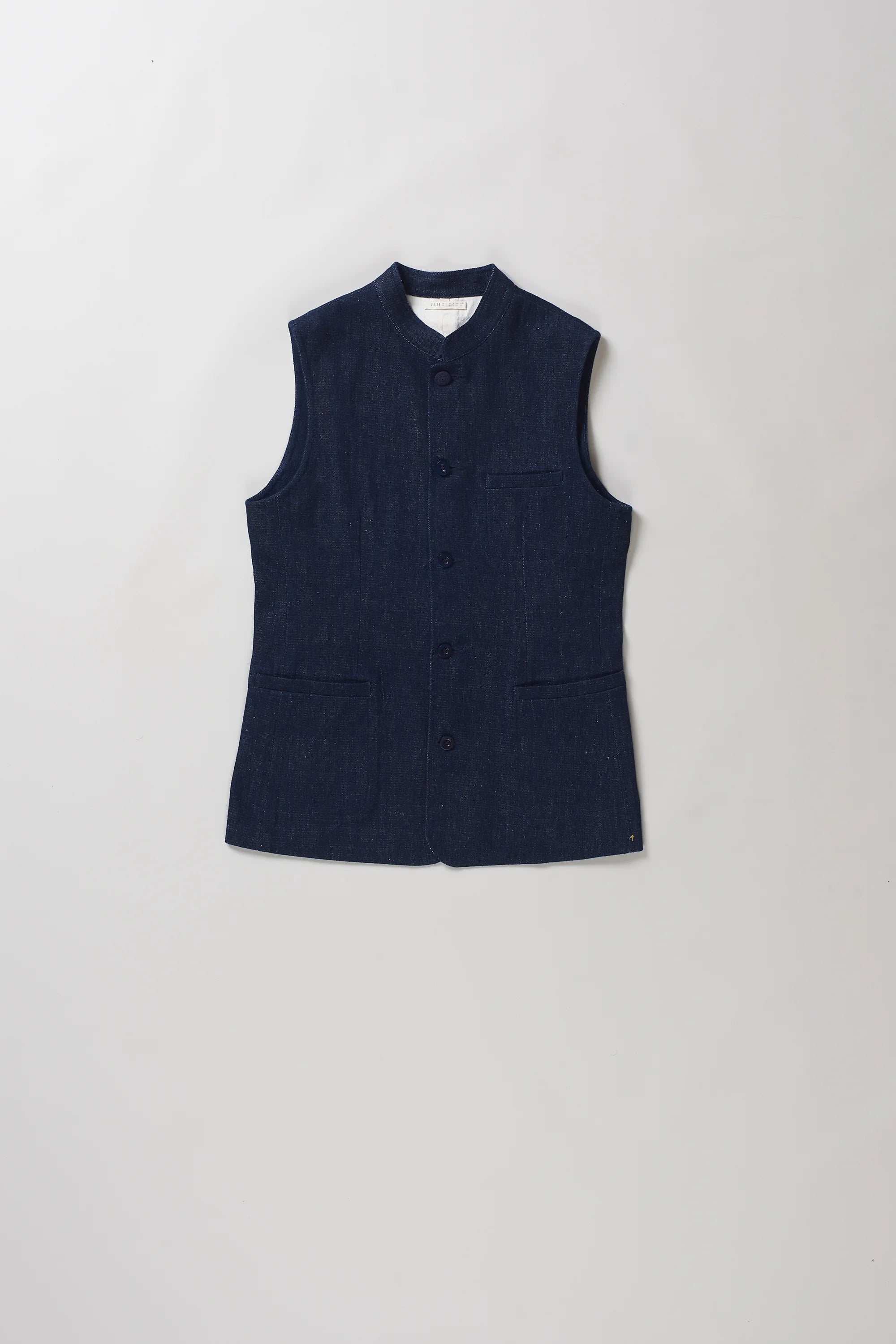 A sleeveless black indigo vest with a mandarin collar and front button closure, laid flat against a light gray background.