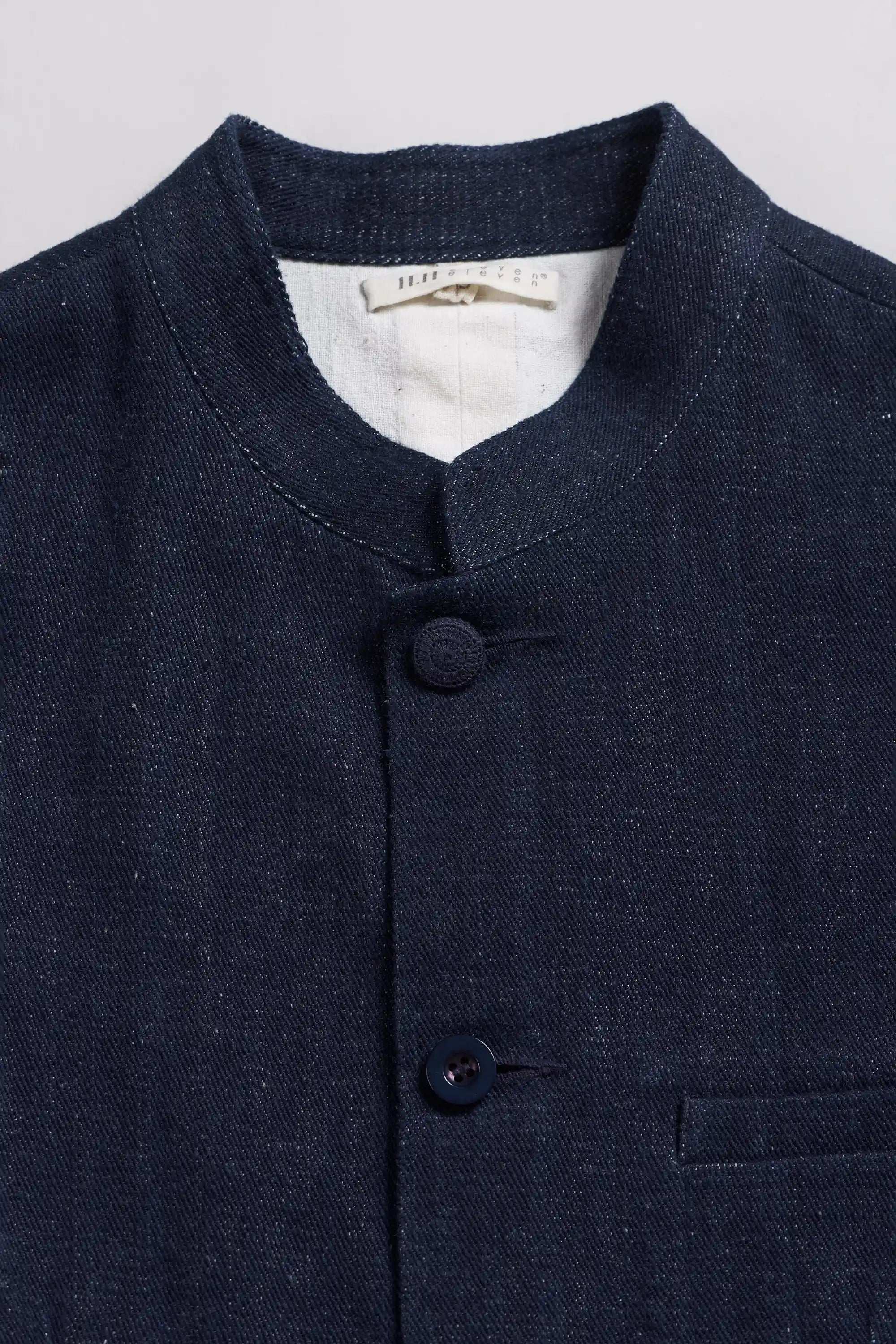 Close-up of a black indigo textured jacket with a mandarin collar and two front buttons, showing a white inner neck label.