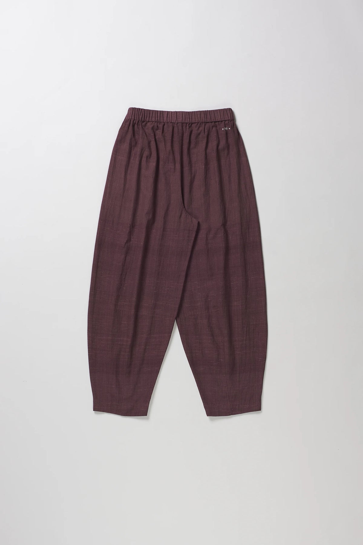 A pair of loose-fitting, pleated trousers in burgundy color, laid flat against a light grey background.