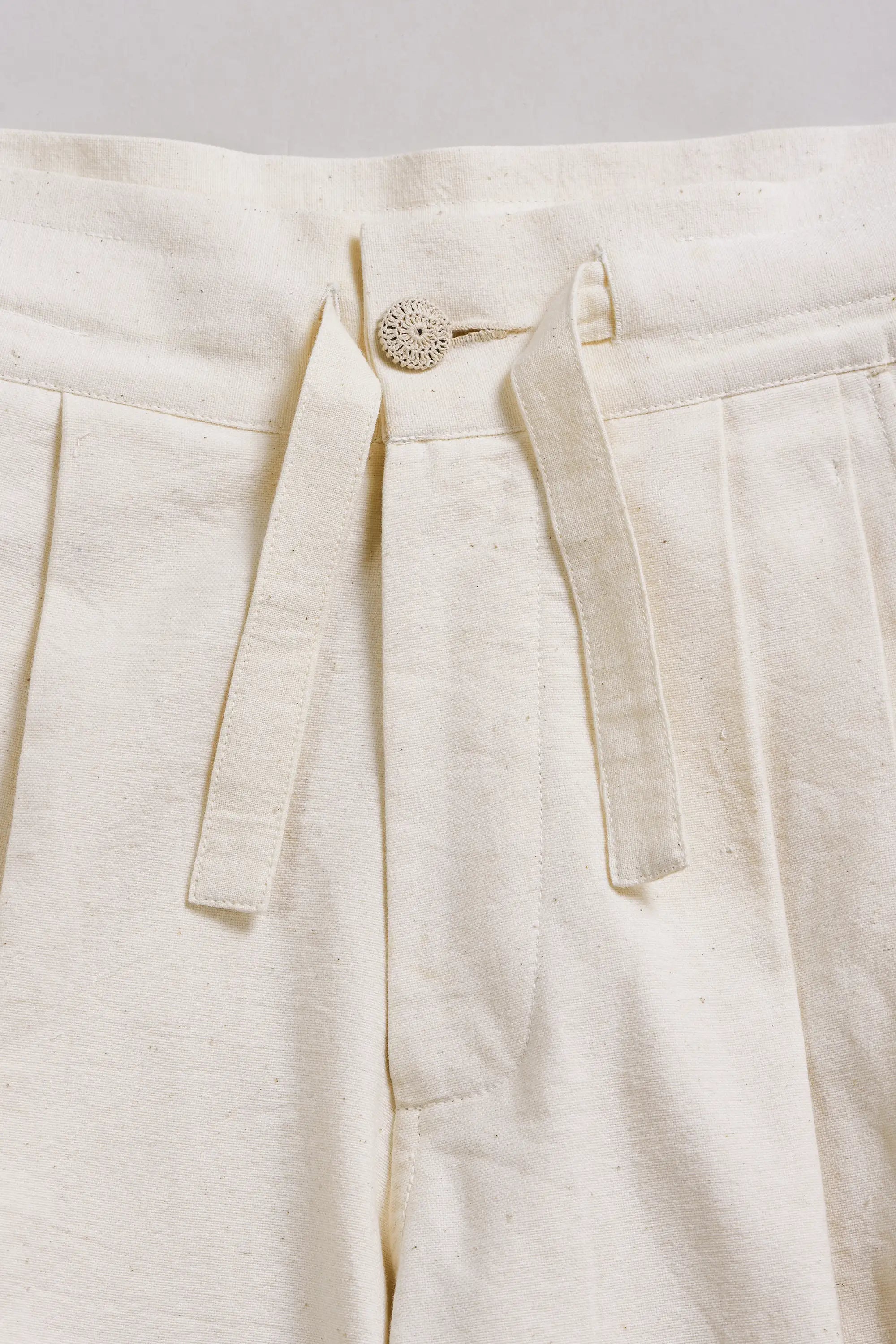 Close-up of a ecru pants with a button on a light grey background