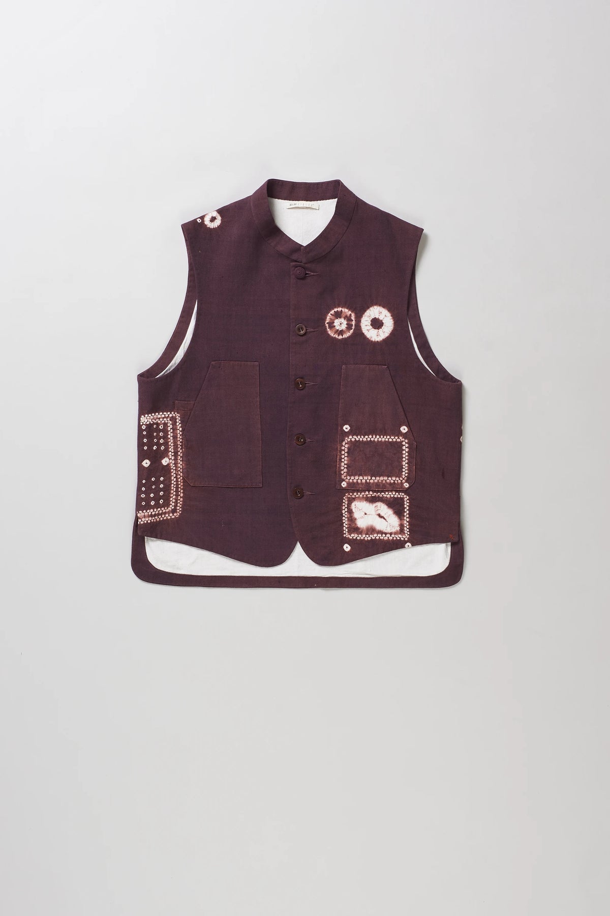 A sleeveless vest with shibori details, button front, and multiple patch pockets, shown flat against a light grey background.