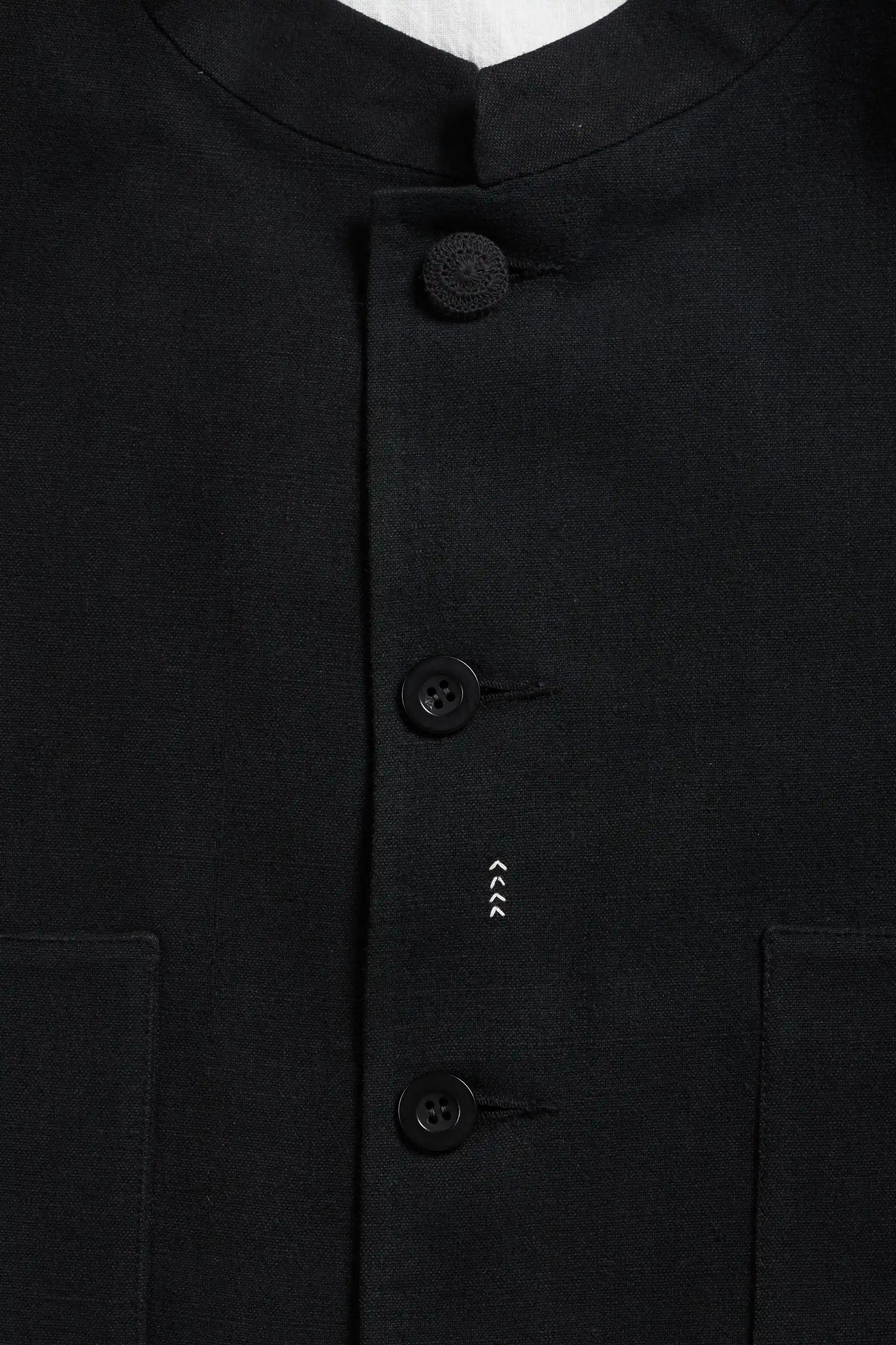 Close-up of a black button-front garment with a stand collar and three visible buttons.