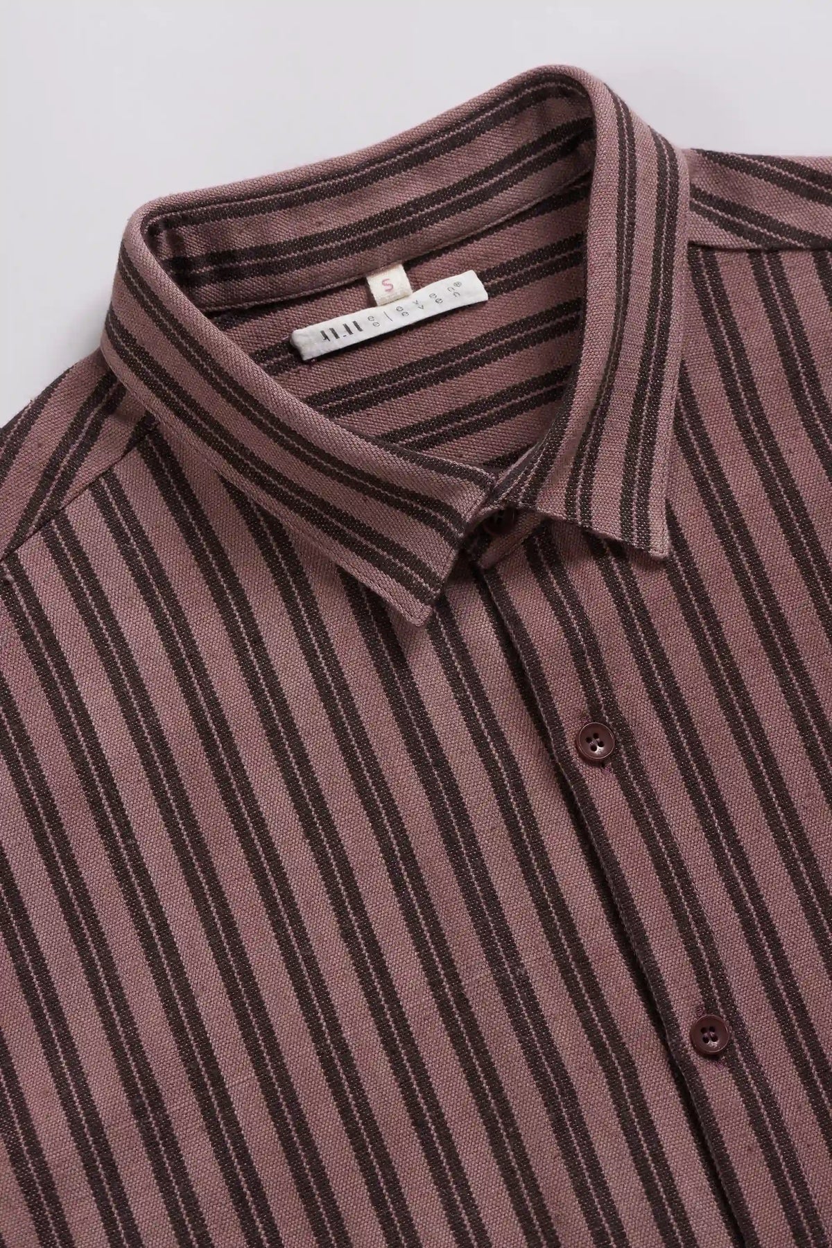 A close-up of a collared button-up shirt with vertical stripes in dusty rose and dark brown, featuring a white neck label.