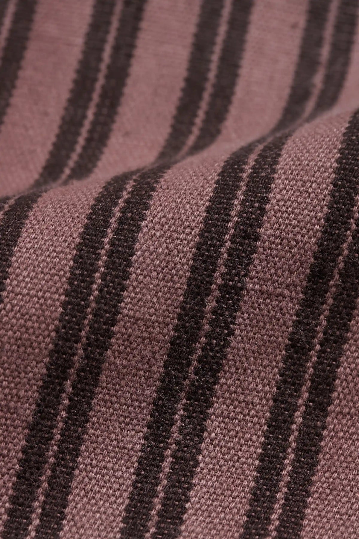 A close-up of a woven fabric with vertical stripes in dusty mauve pink and dark brown.