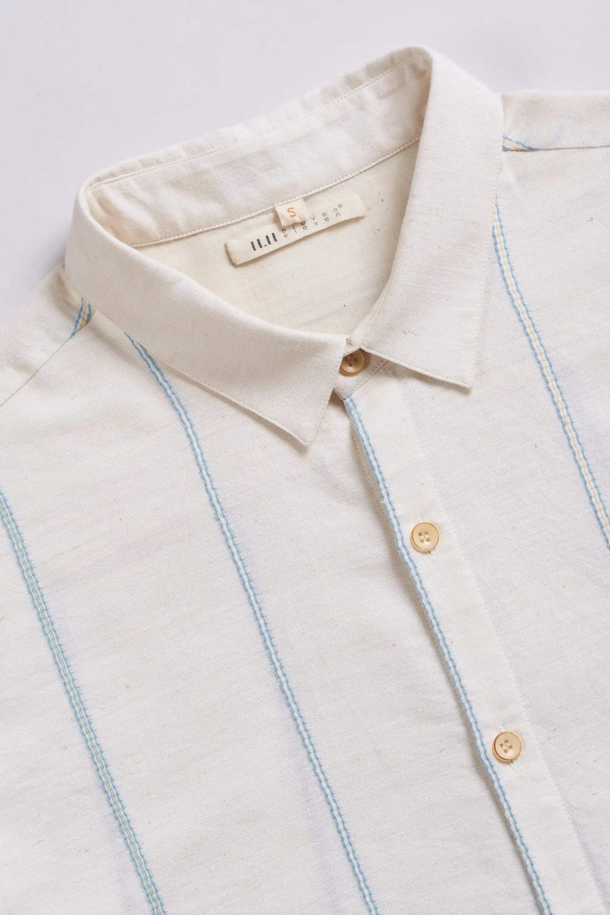 Close-up of a white shirt with yarn dyed and gold buttons on a light grey background