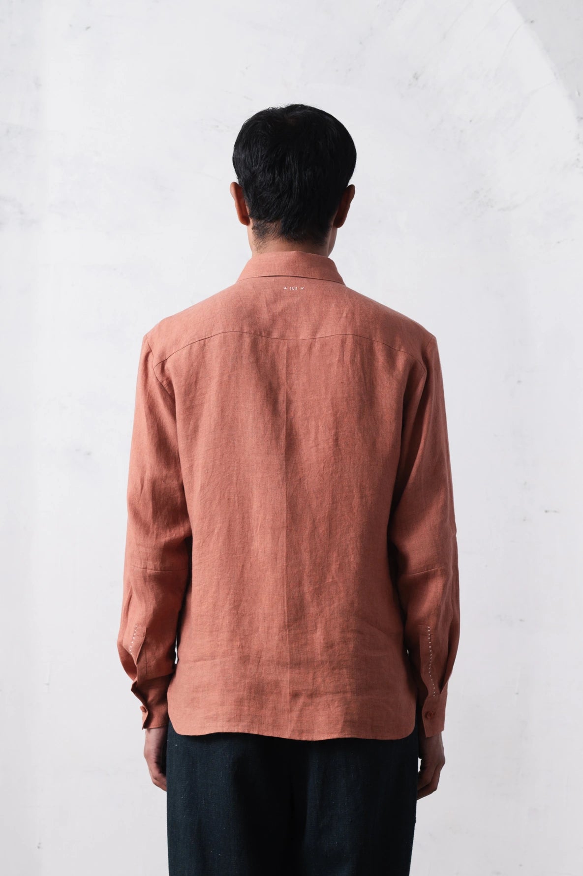 Back shot of a person wearing a orange rust shirt against a light grey background