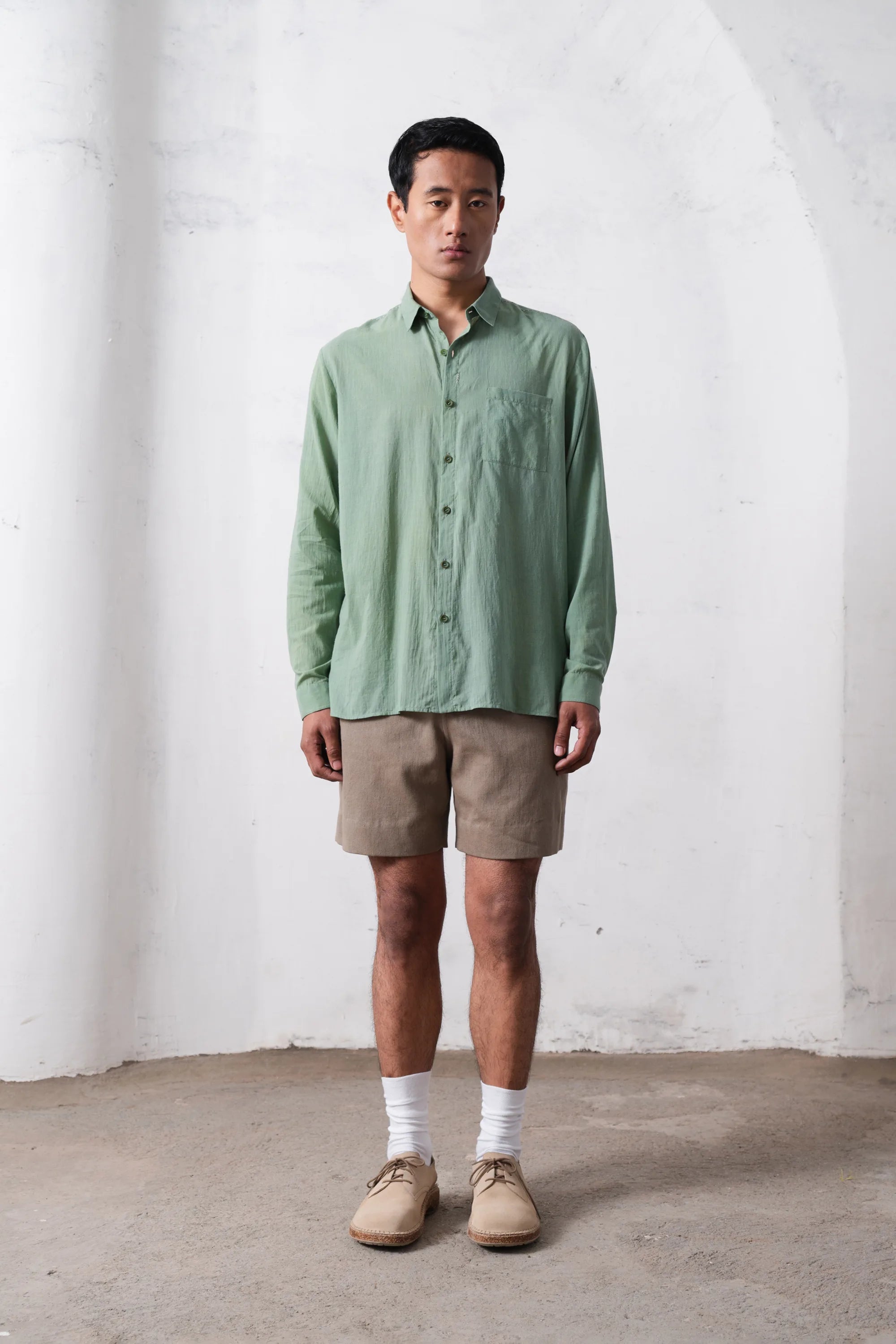 Man wearing a green shirt and beige shorts against a light grey wall