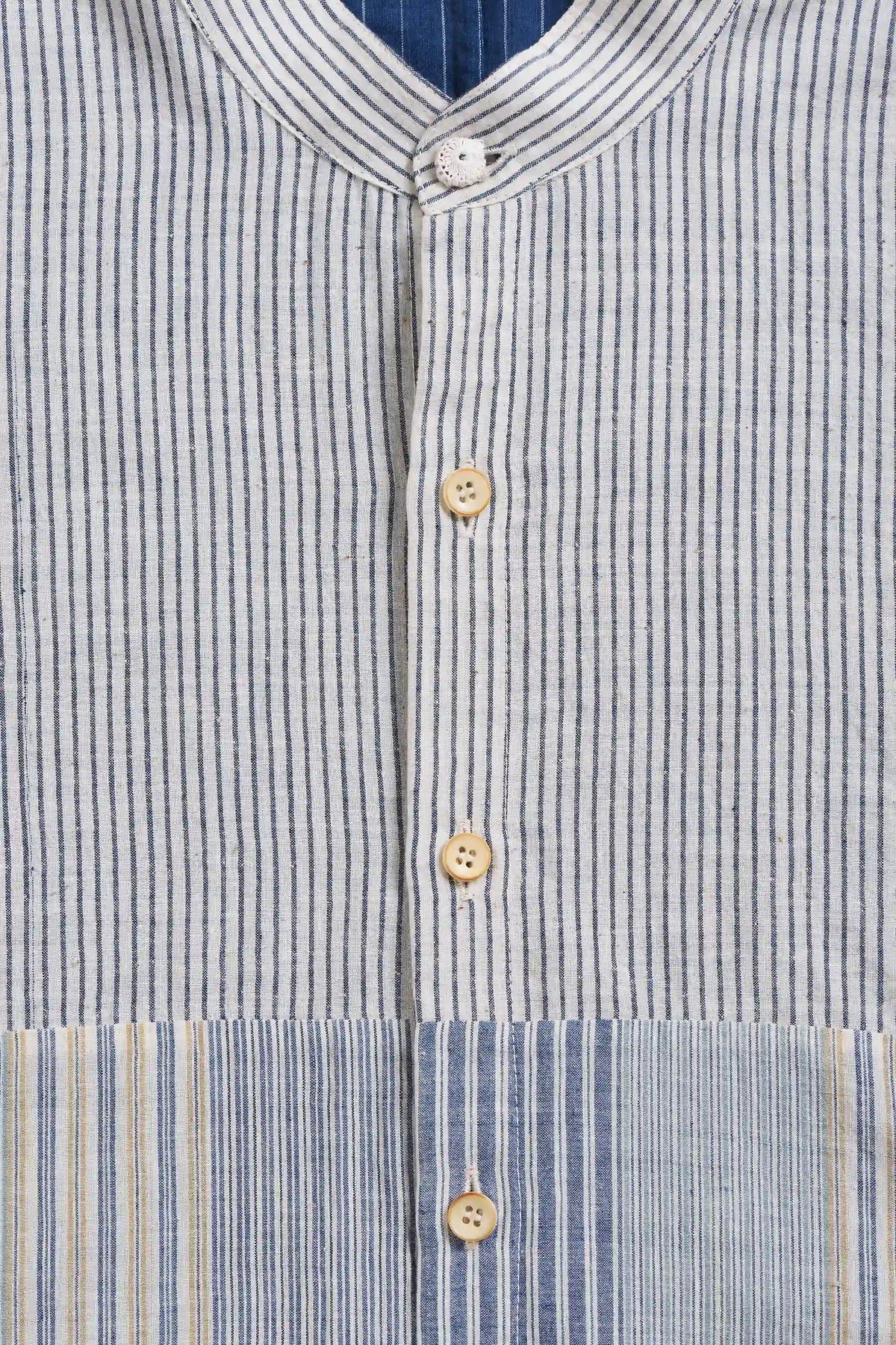 Close-up of a striped button-front shirt with a stand collar and light wood buttons, showing vertical blue, white, and beige stripes.