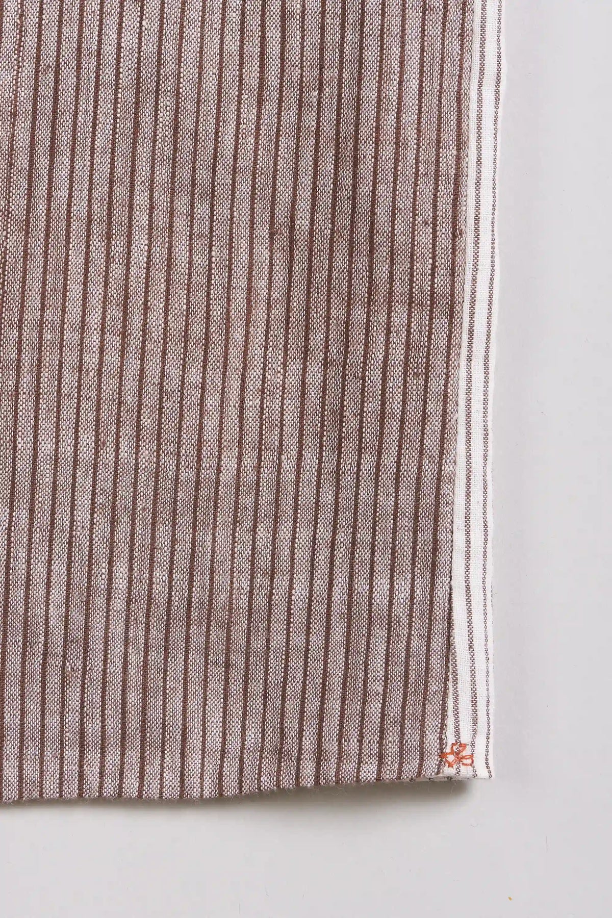 A close-up of a fabric and a small red embroidered logo near the corner, shown against a grey background.