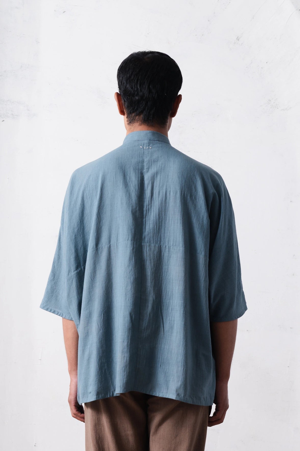 Back shot of a person wearing a light blue shirt from behind on a light grey background