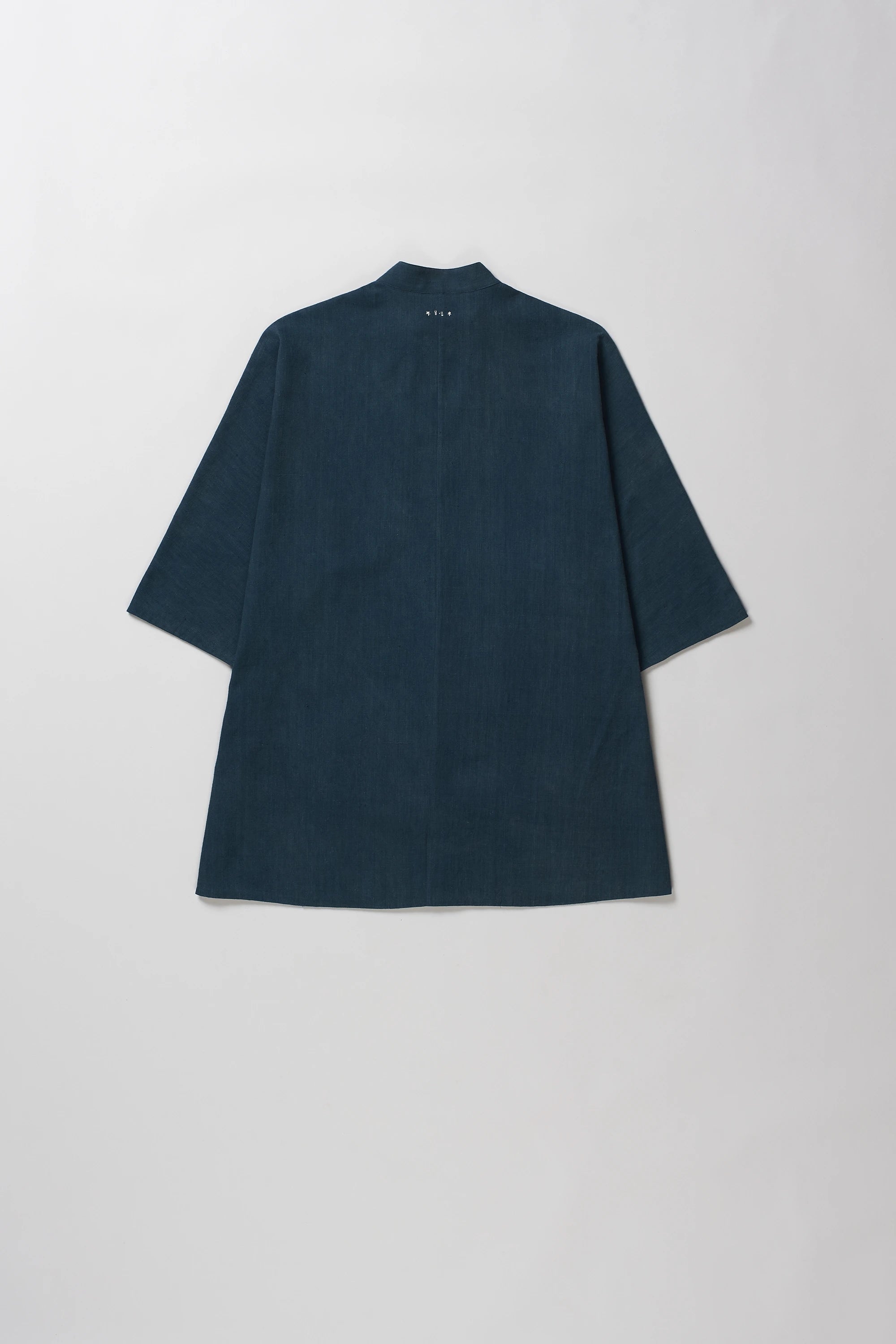 Back shot of half-sleeve button-up shirt with a band collar, laid flat against a light gray background.