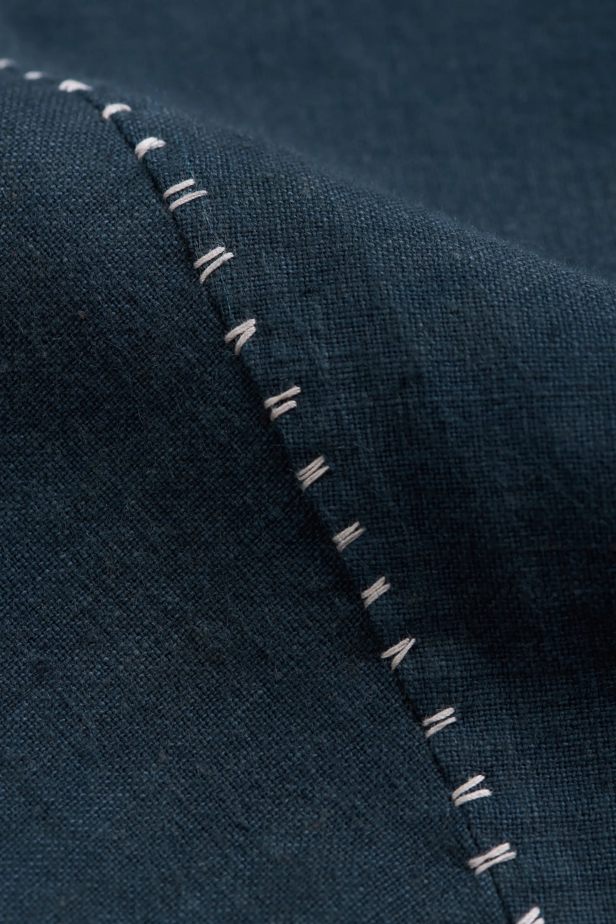 Close-up of black indigo fabric with a diagonal white stitched seam.