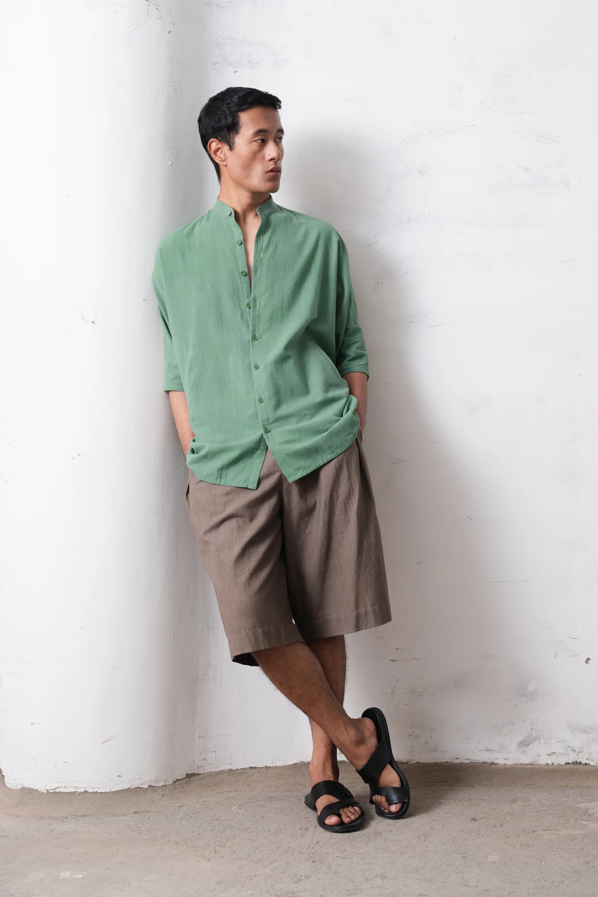 Man wearing a green shirt and brown shorts against a light grey wall