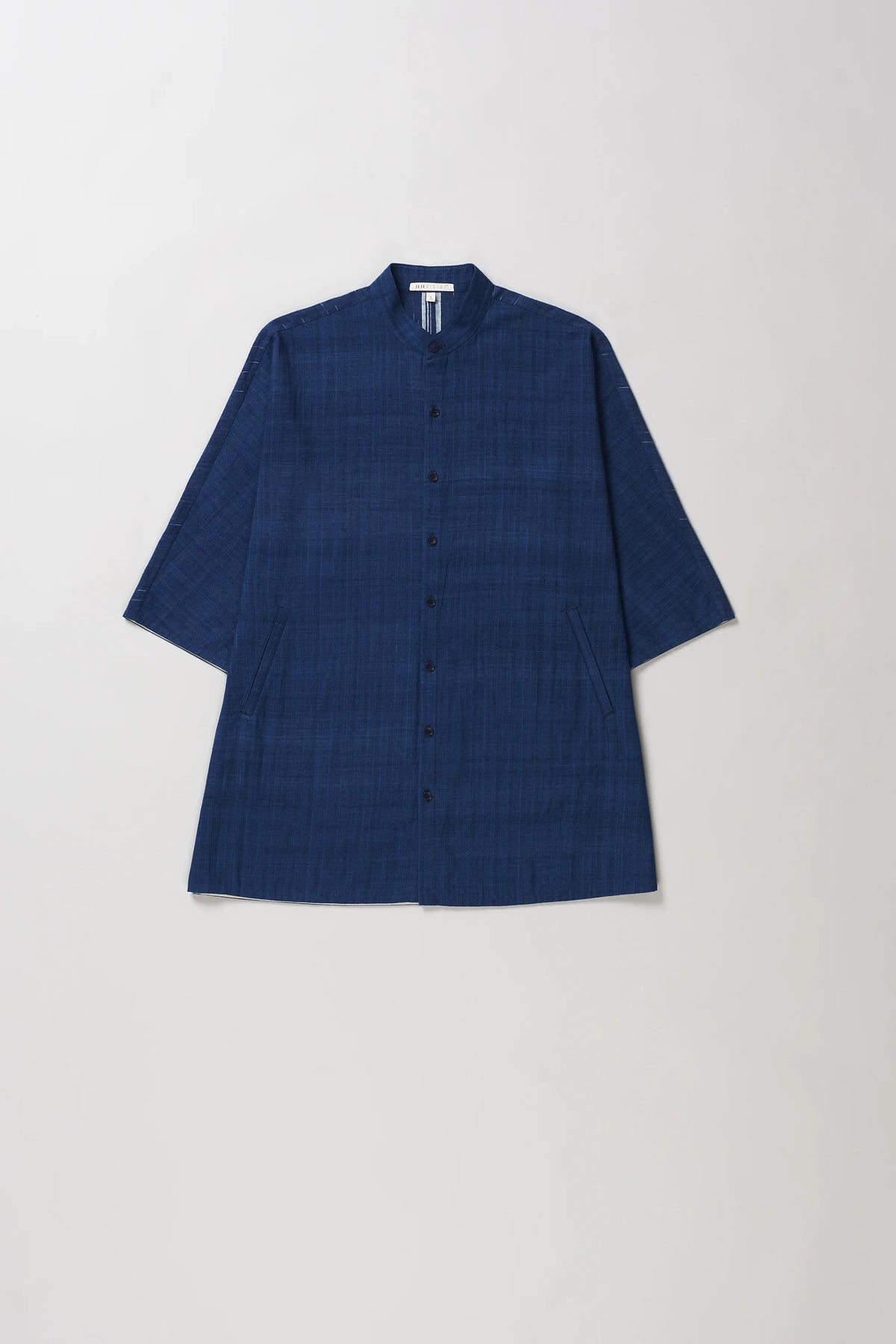 A indigo textured button-up shirt with a mandarin collar and three-quarter sleeves, laid flat against a light grey background.