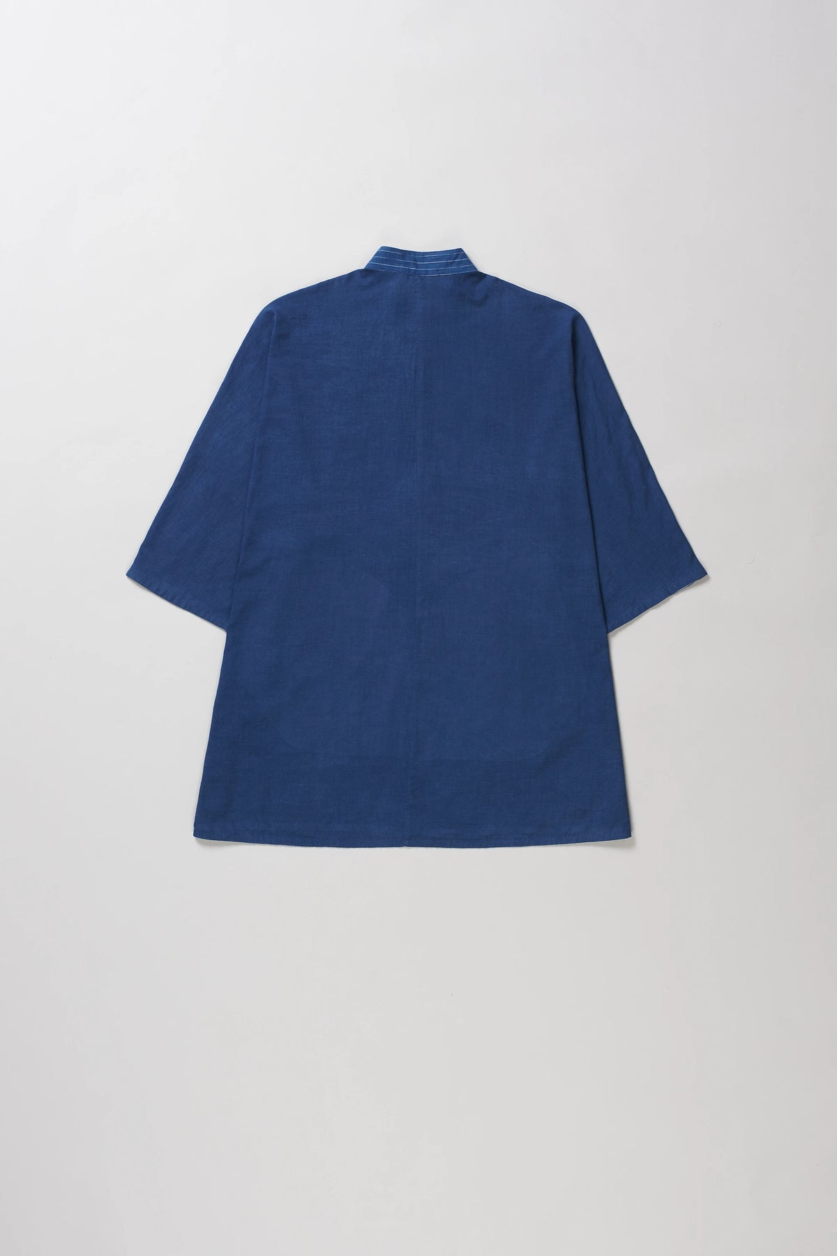 A indigo short-sleeve shirt with a high collar, shown from the back against a light grey background.